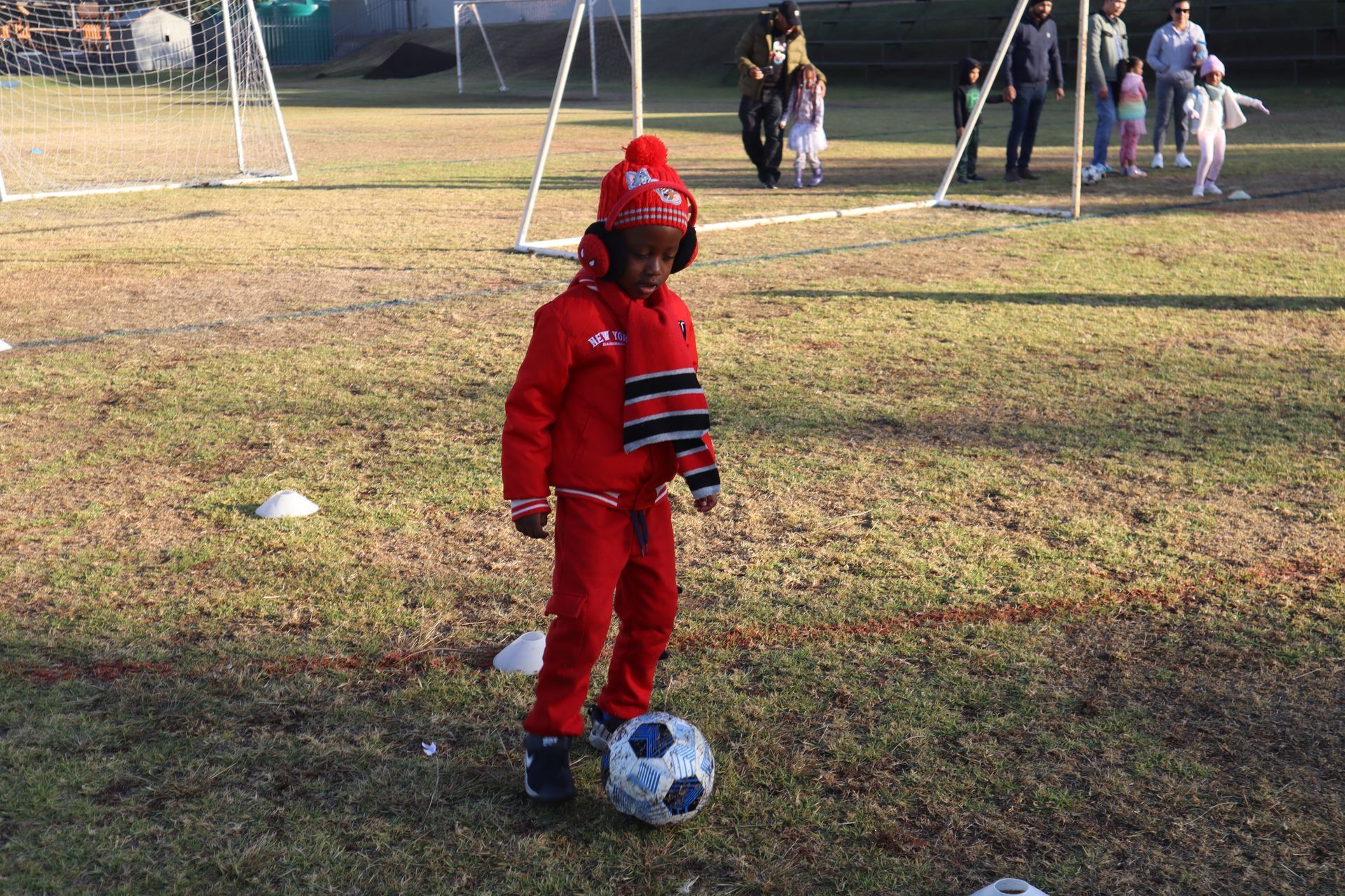 A little boy in a red outfit is kicking a soccer ball on a field.