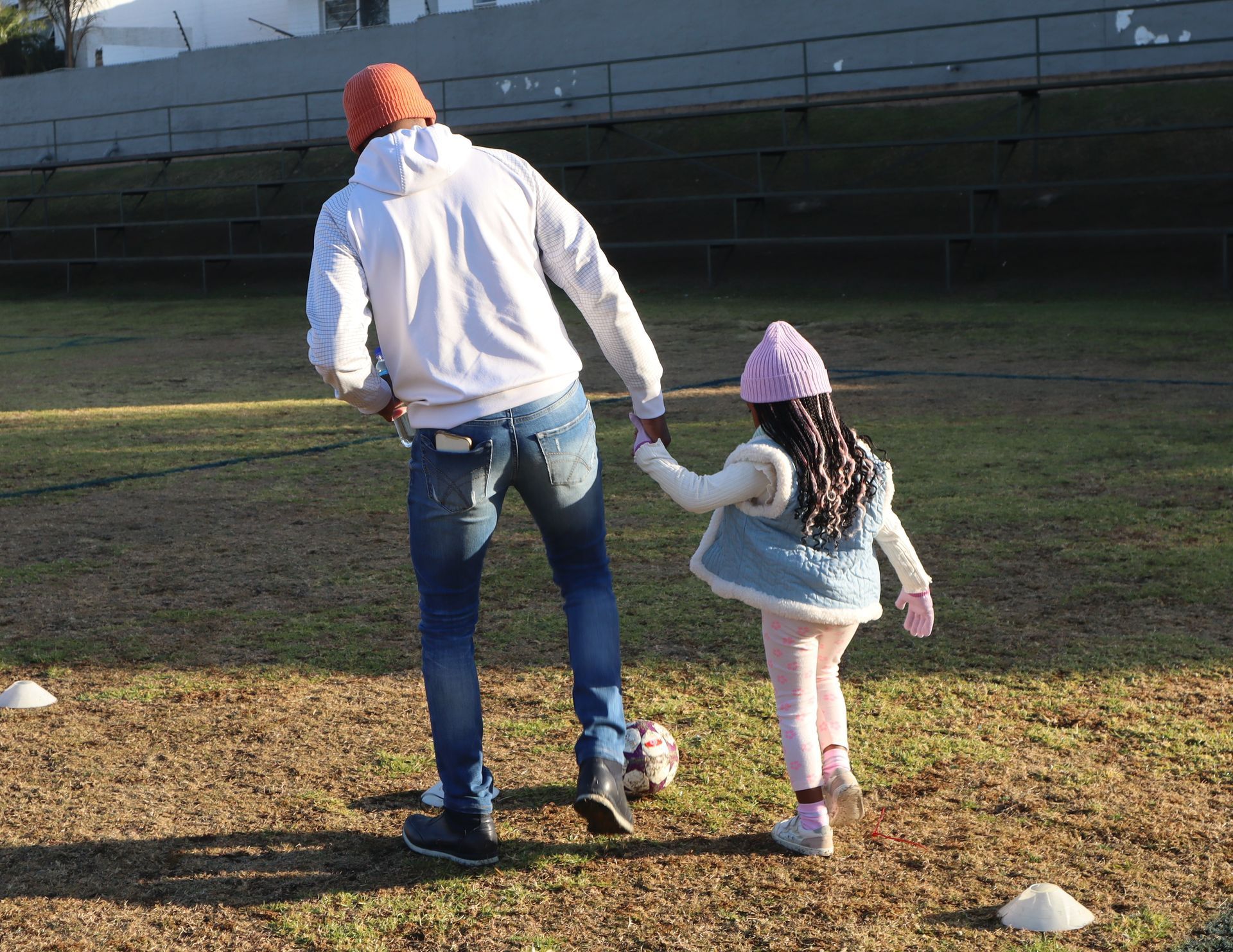 A man and a little girl are walking on a field holding hands