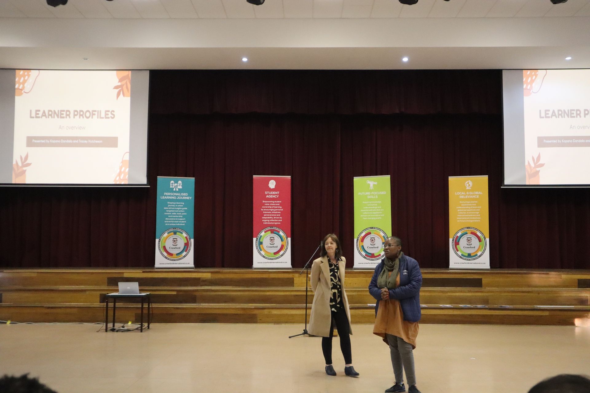 Two women are standing on a stage in front of a large screen.