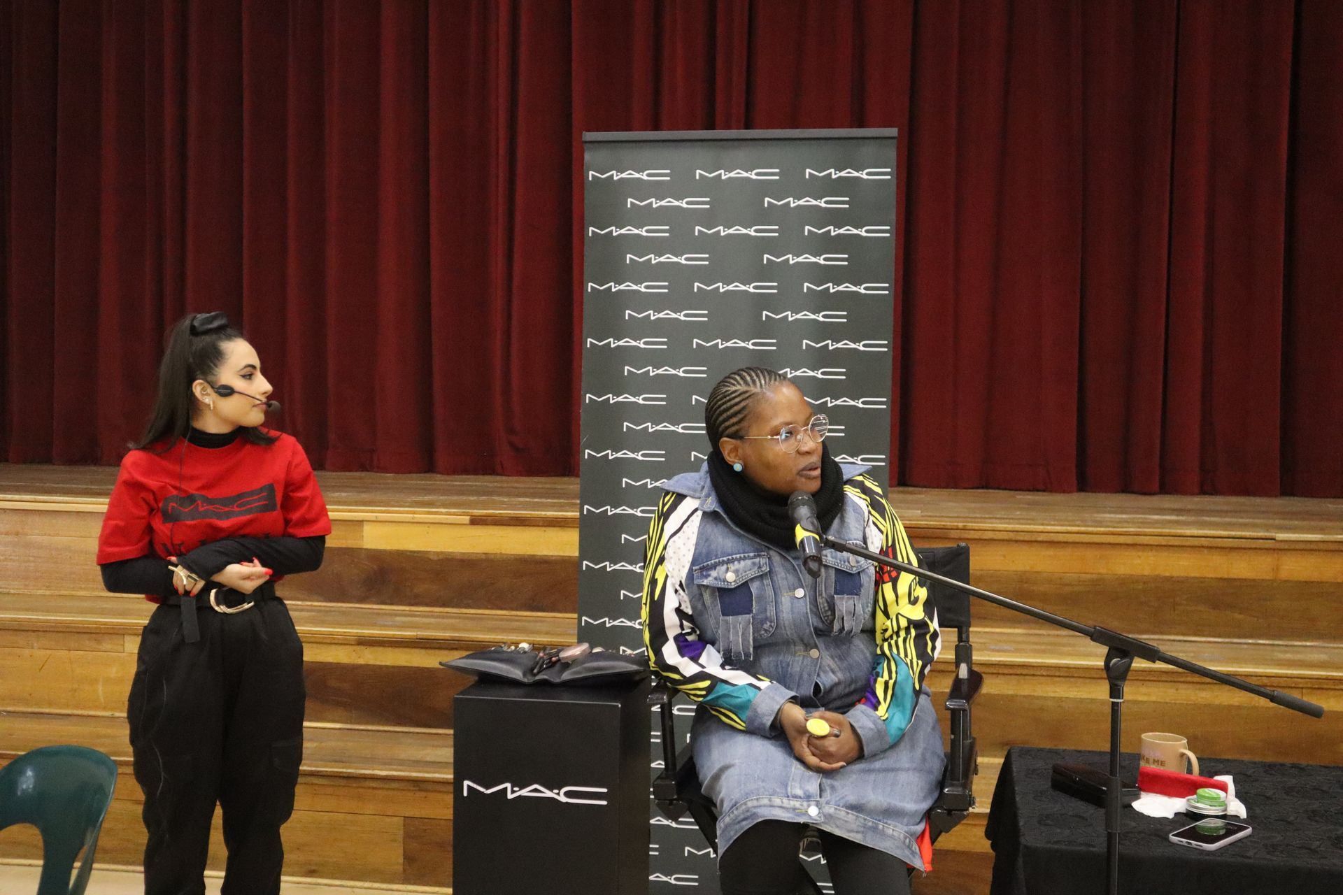 Two women are standing next to each other on a stage in front of a microphone.
