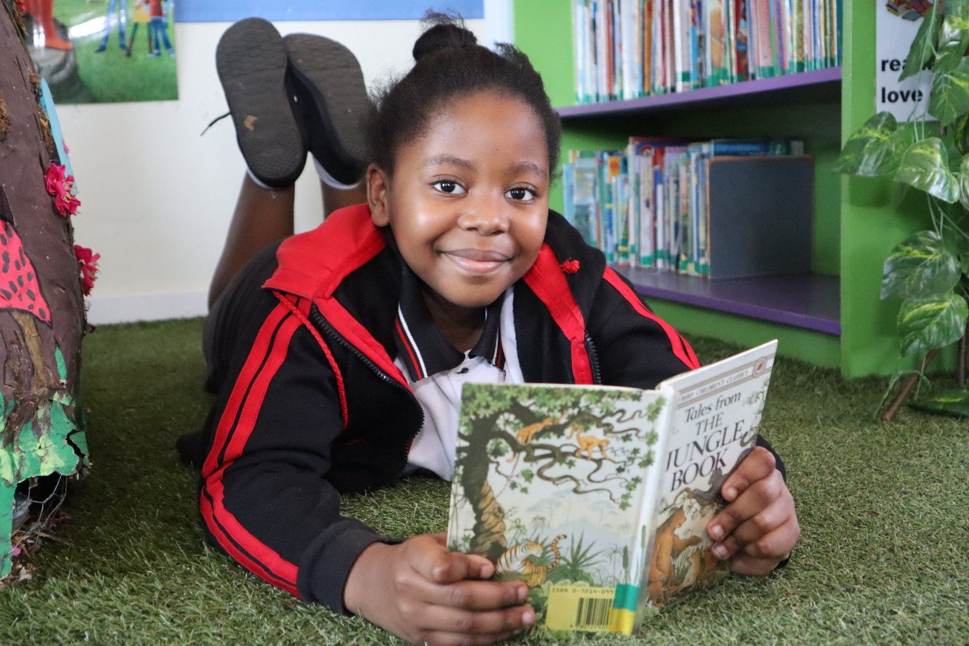 a young girl is laying on the floor reading a book .