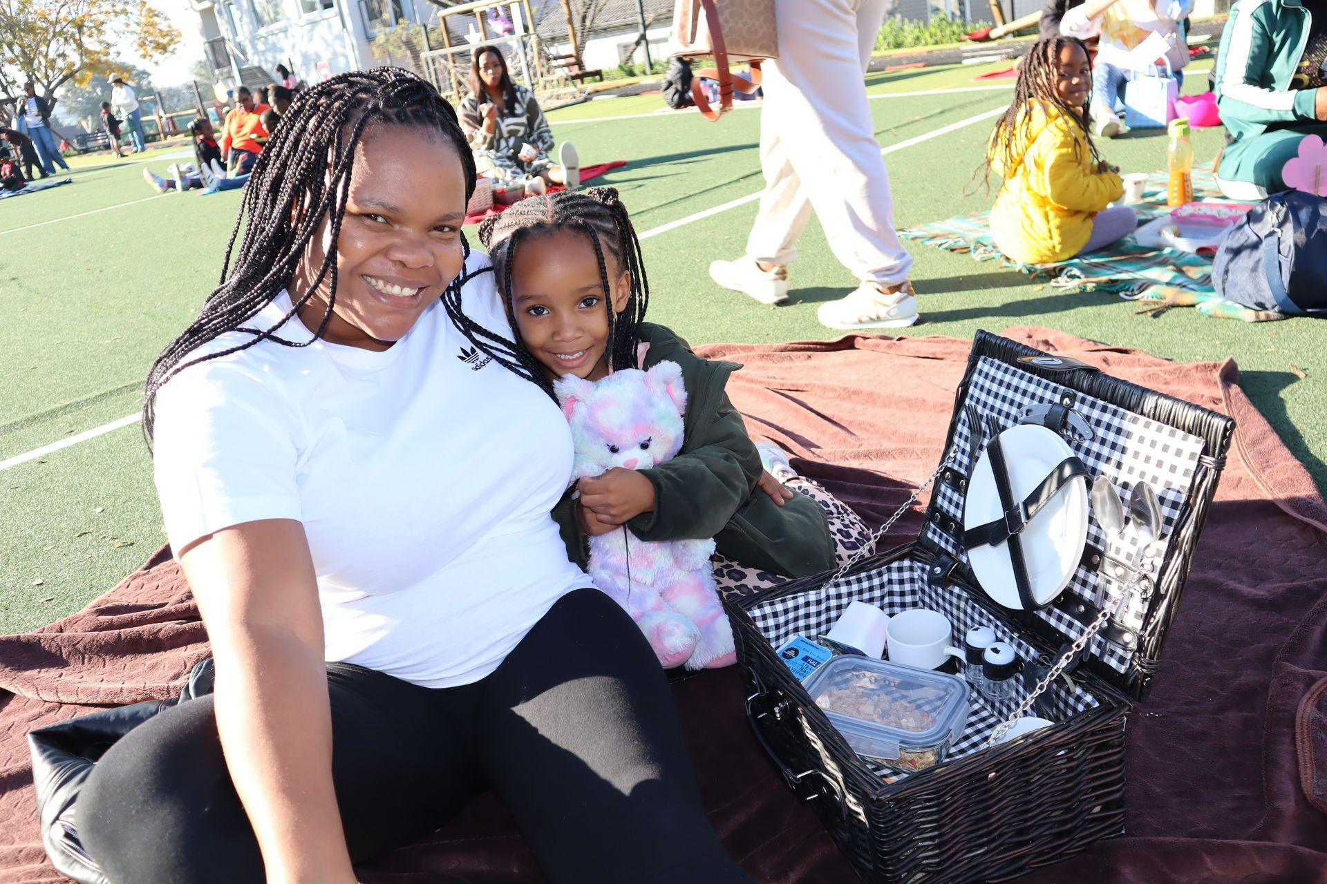 Woman and child smiling at the camera during a picnic; open picnic basket in front.