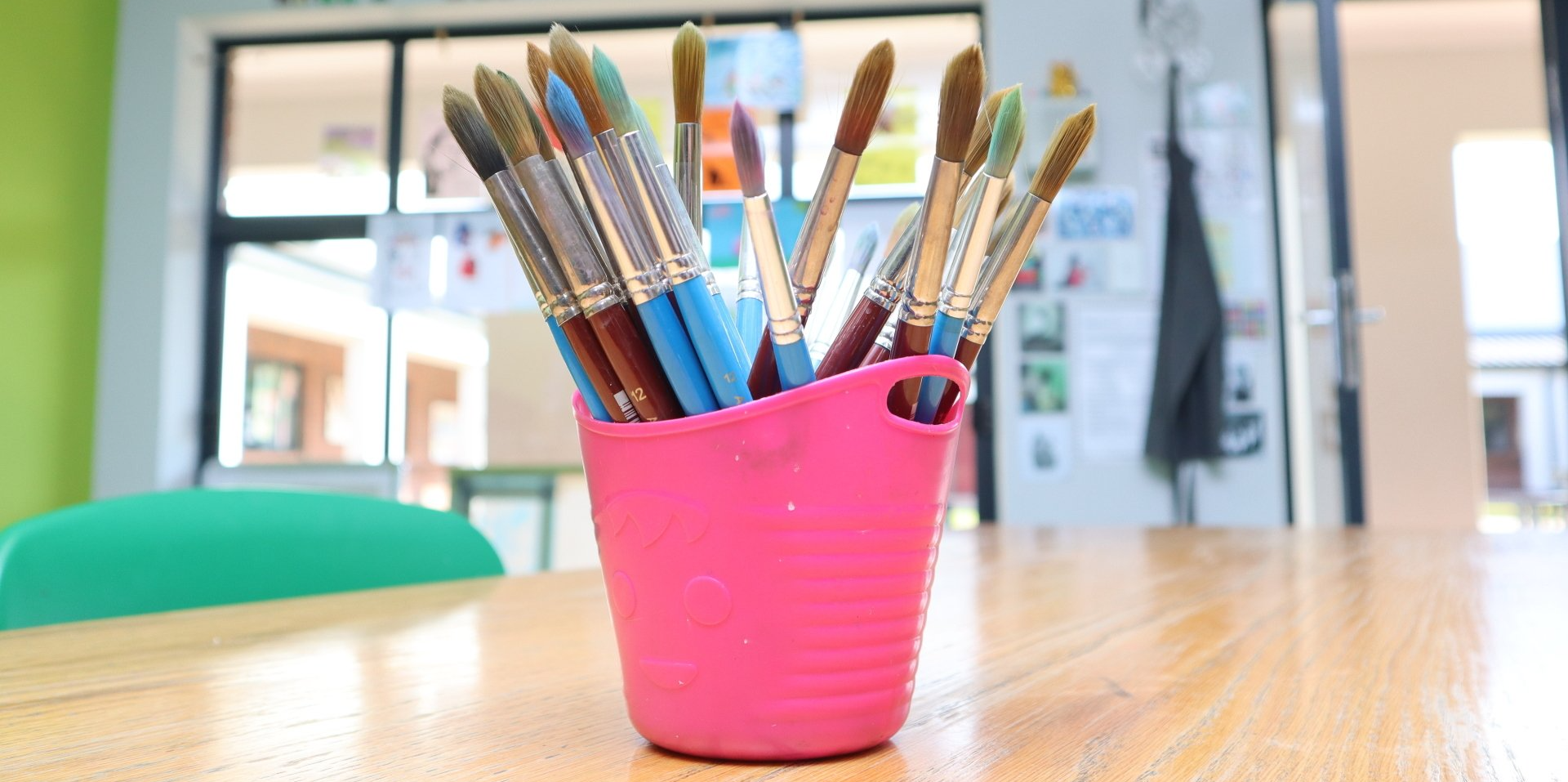 a pink bucket filled with paint brushes is sitting on a wooden table .