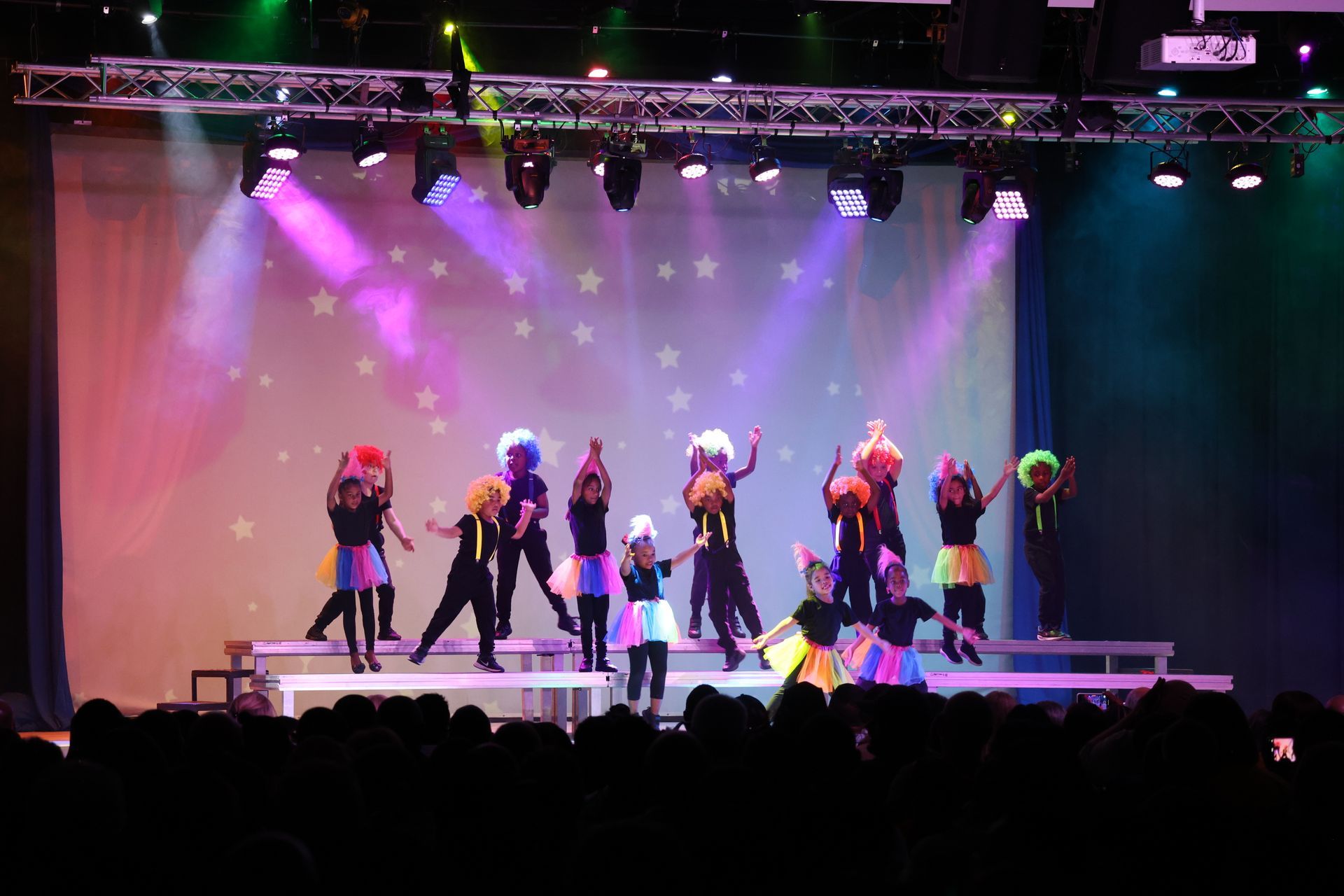 A group of children are dancing on a stage in front of a crowd.