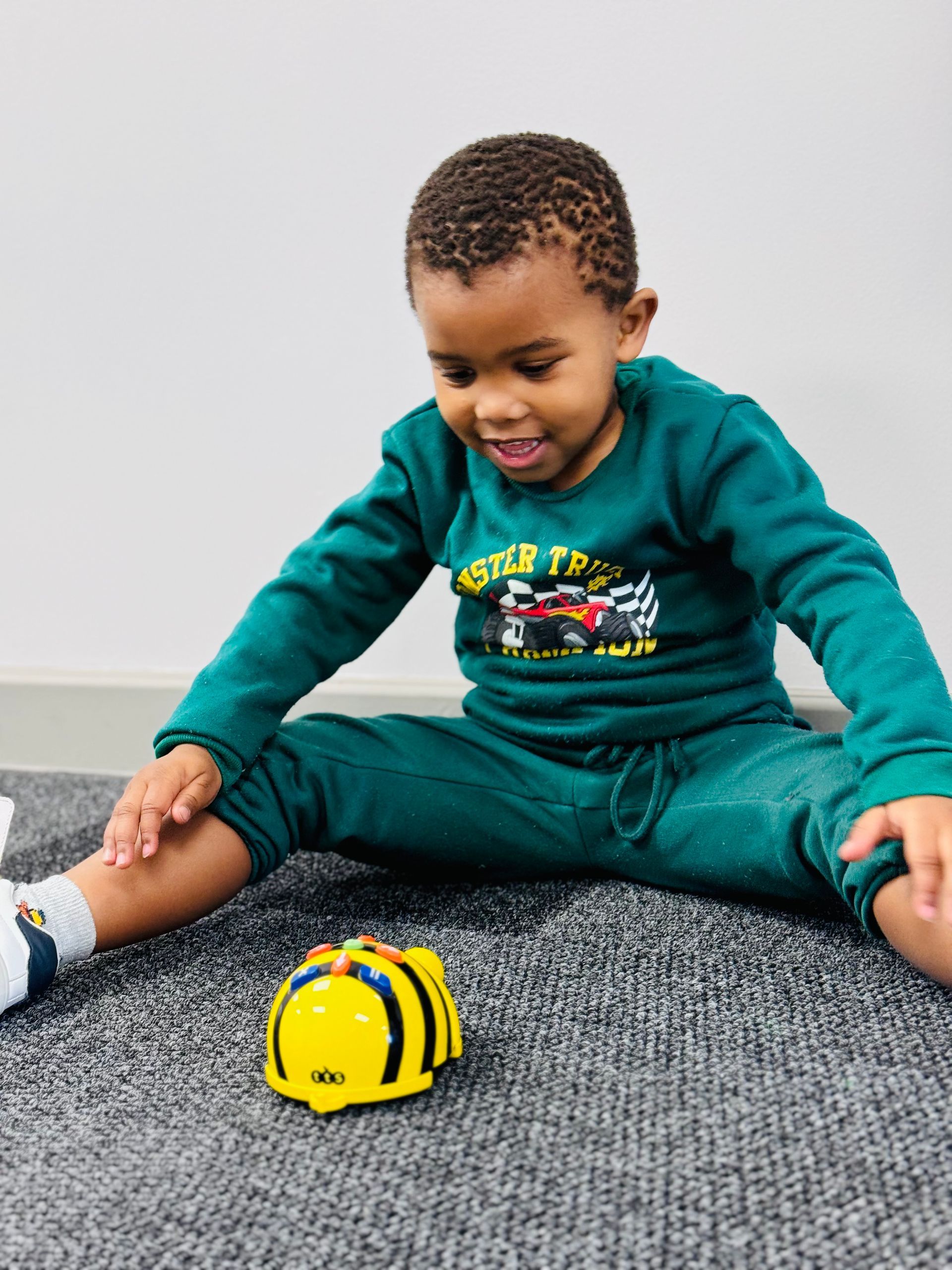 A young boy is sitting on the floor playing with a yellow toy.