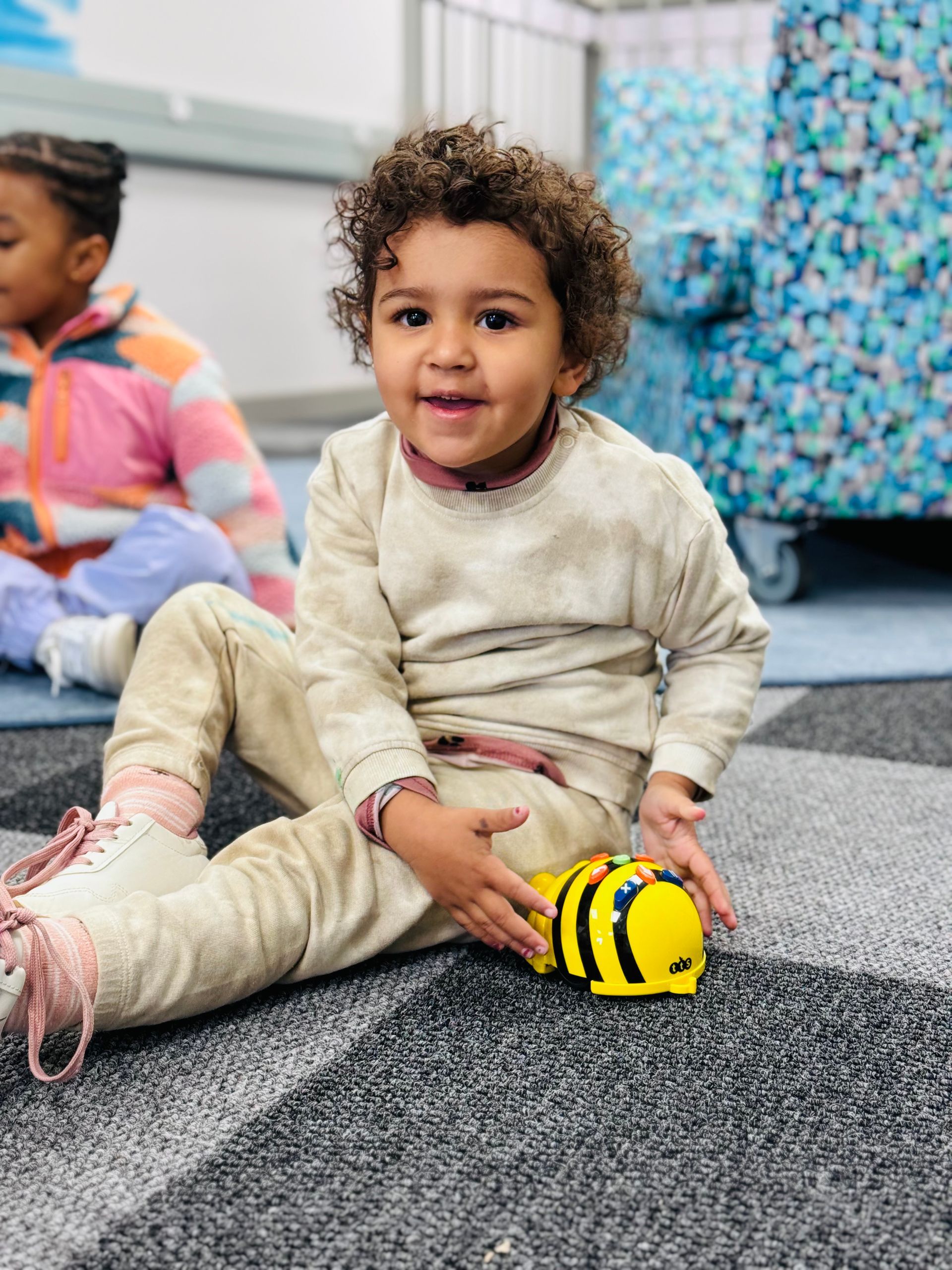 A young boy is sitting on the floor holding a toy bee.