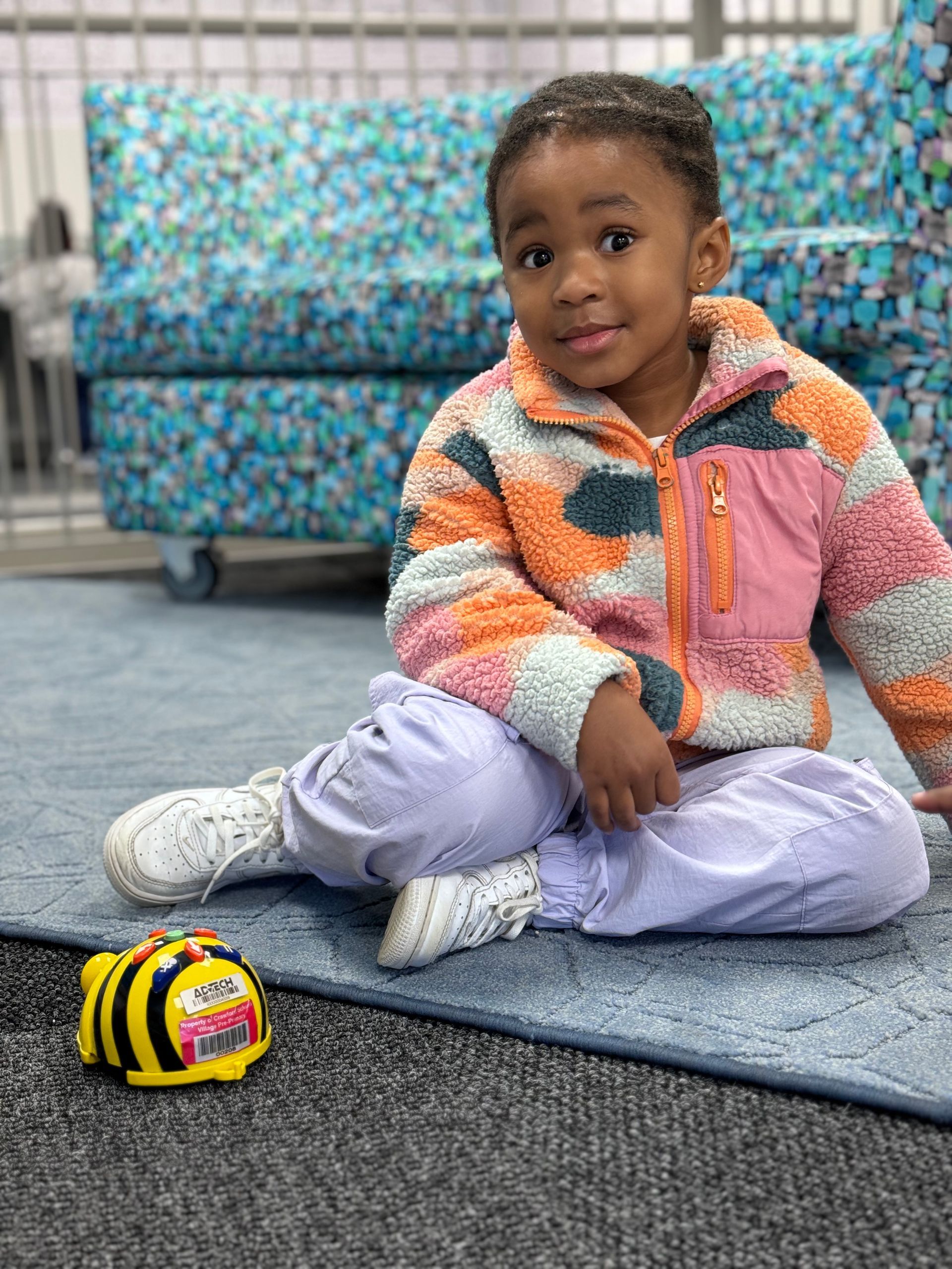 A little girl is sitting on the floor next to a toy bee.
