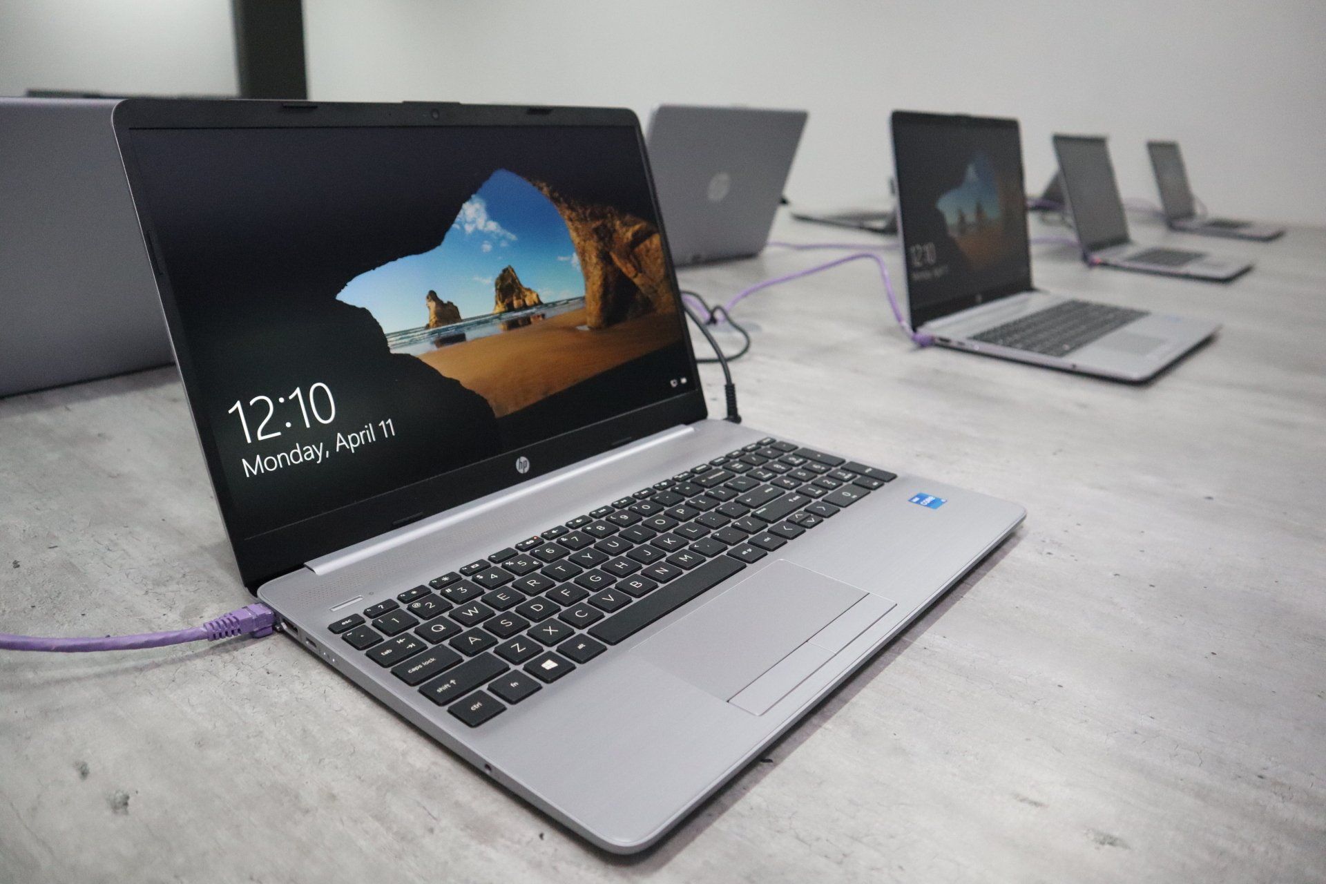 a row of laptops are sitting on a table and one of them says 12:10 on the screen