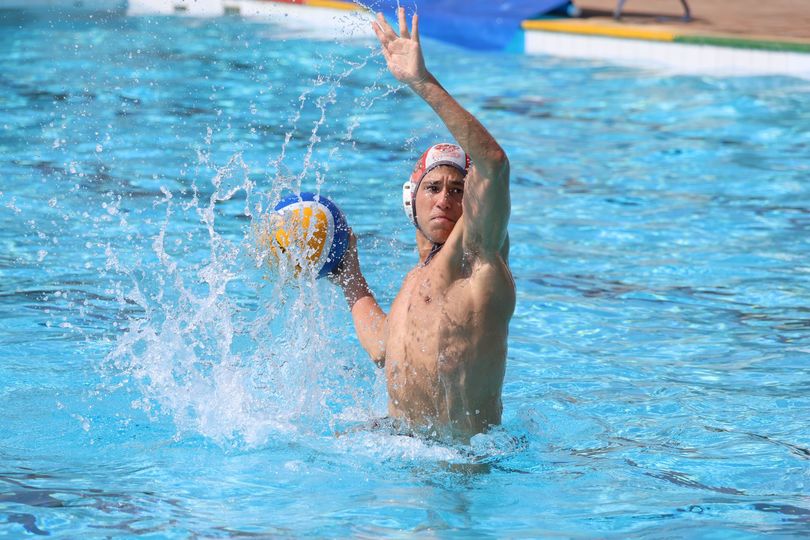 Water polo player throwing ball in pool, with water splashing.