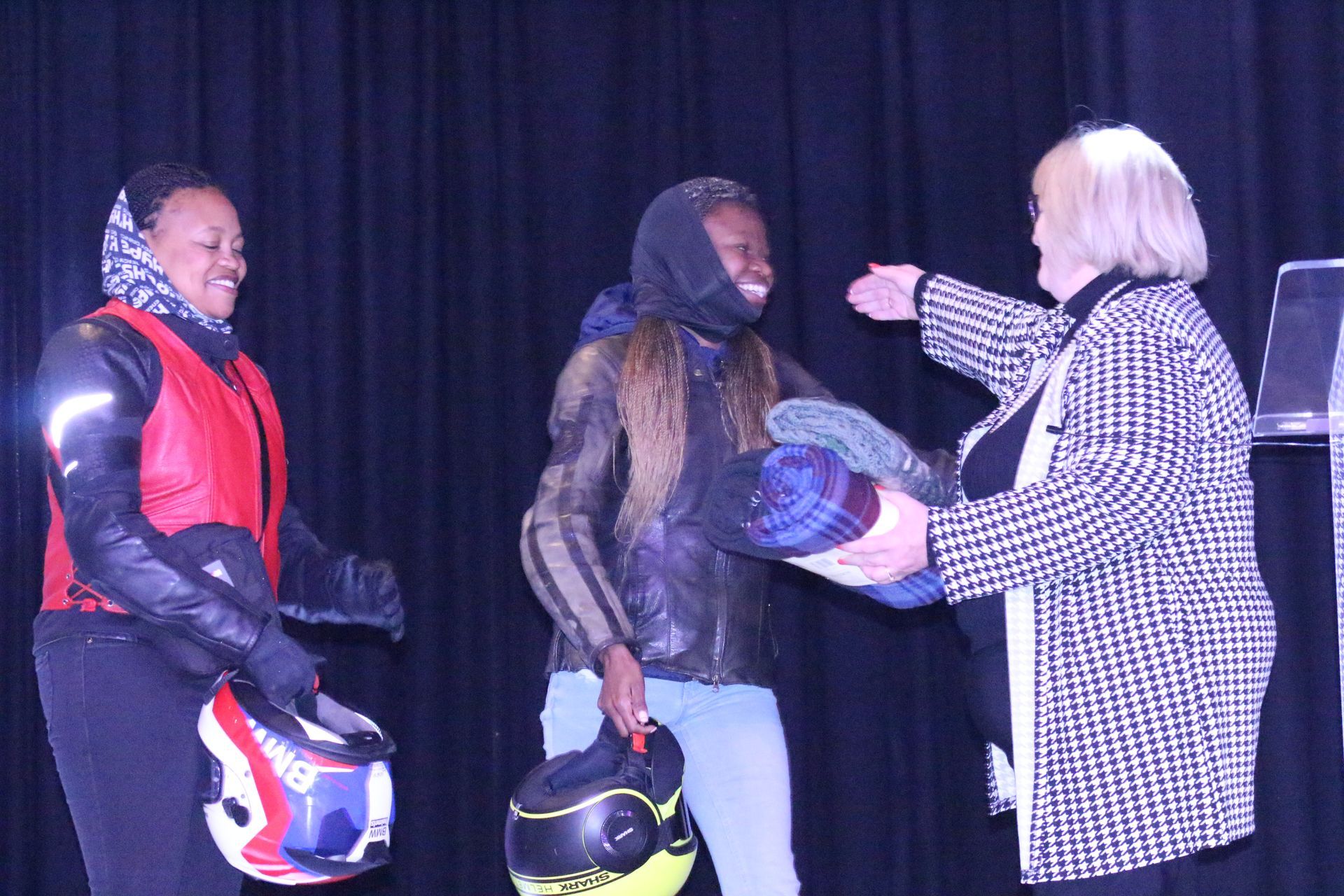 A woman is giving a helmet to a man on a stage.
