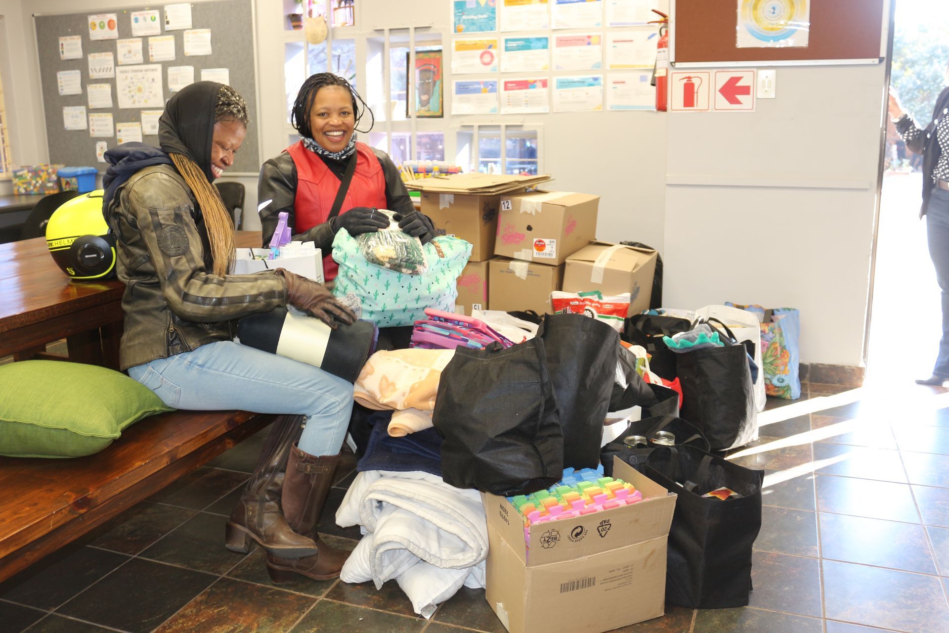 Two women are sitting on a bench next to a pile of boxes.