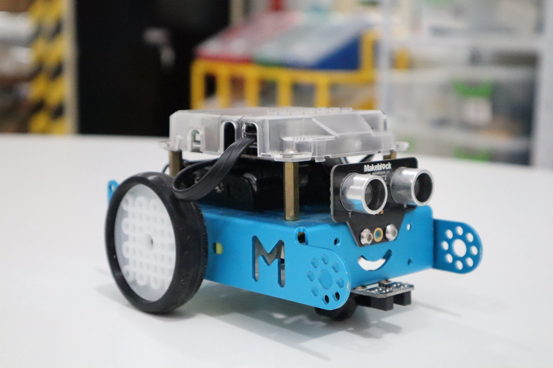 A blue robot with the letter m on it is sitting on a table.