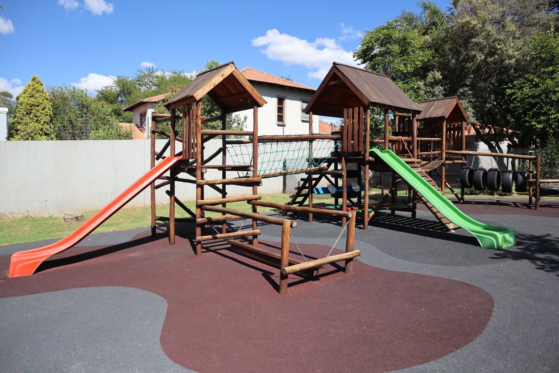a wooden playground with a green slide and a red slide