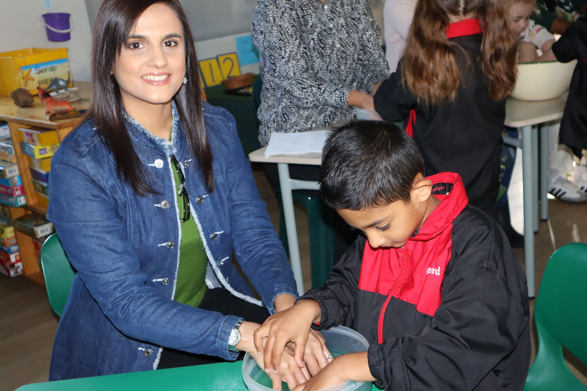 Woman assisting a student with a sensory activity in a classroom.
