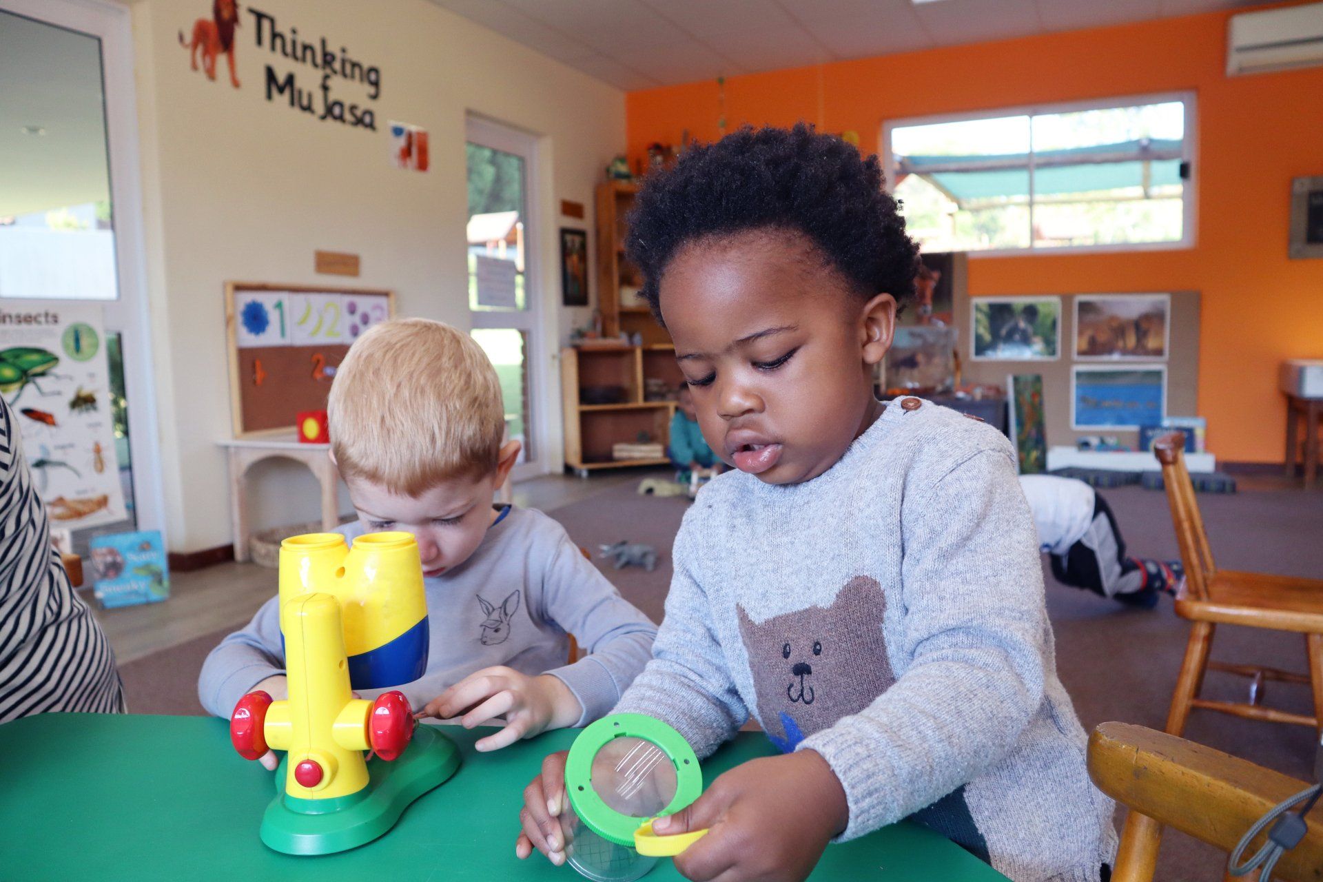 two young children are playing with toys at a table in a classroom