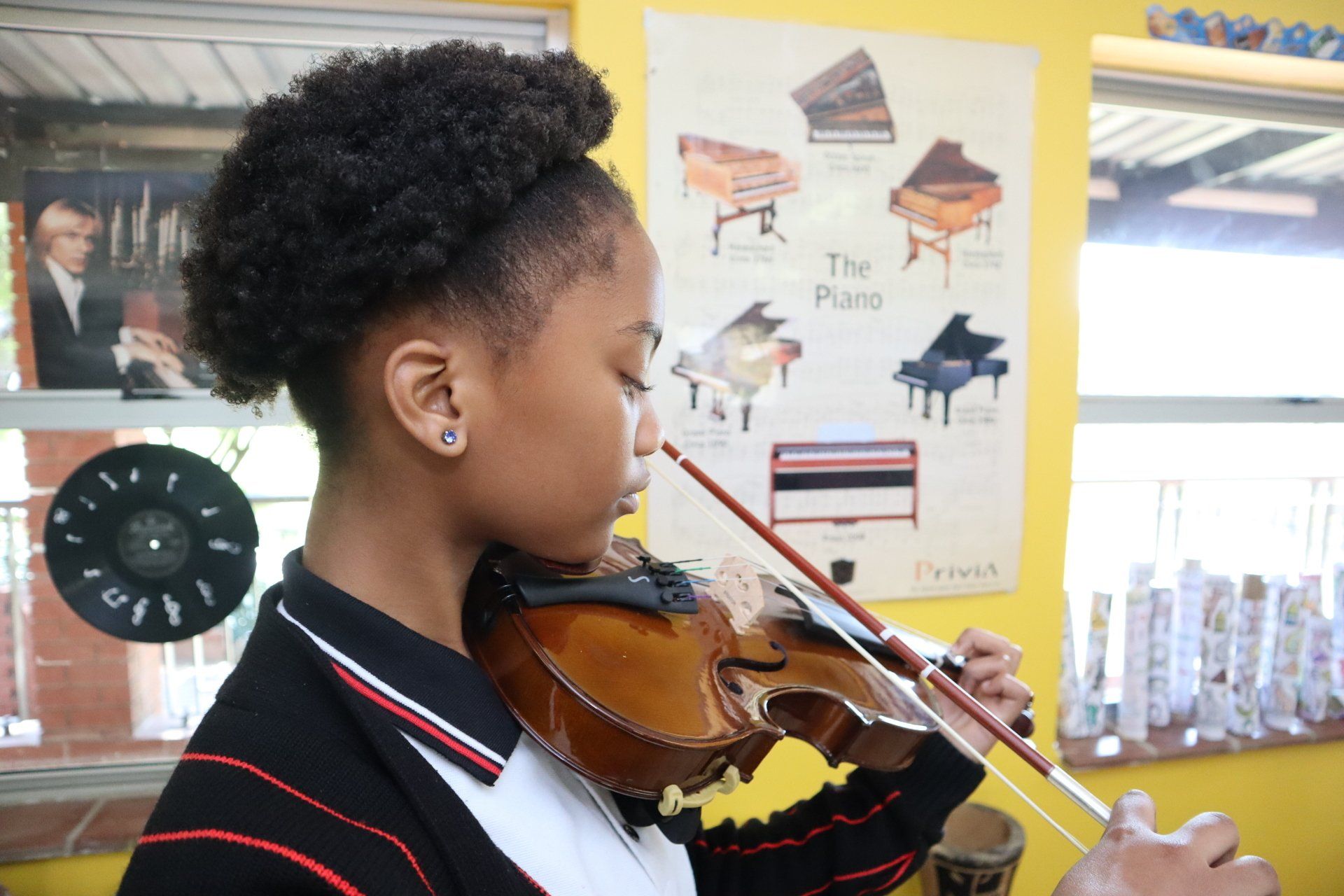 A young girl is playing a violin in front of a poster of pianos