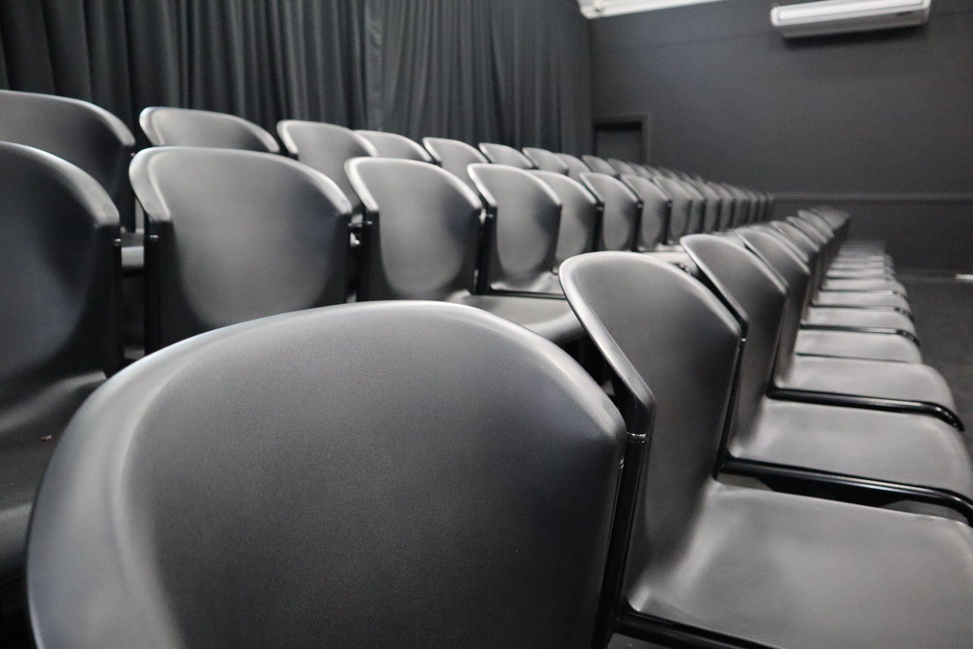 rows of empty chairs in an auditorium with a black curtain
