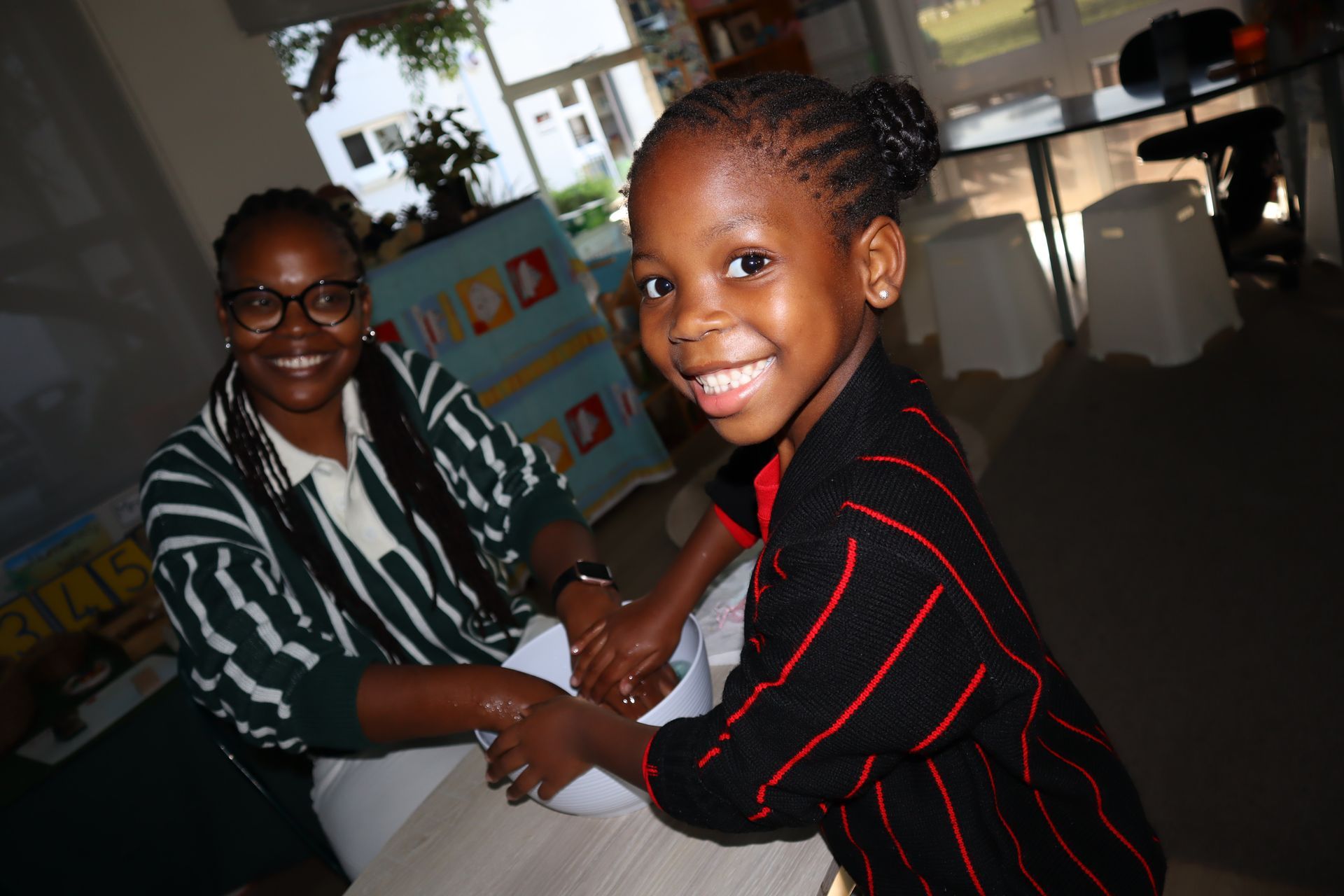 Woman helping child wash hands; both smiling.