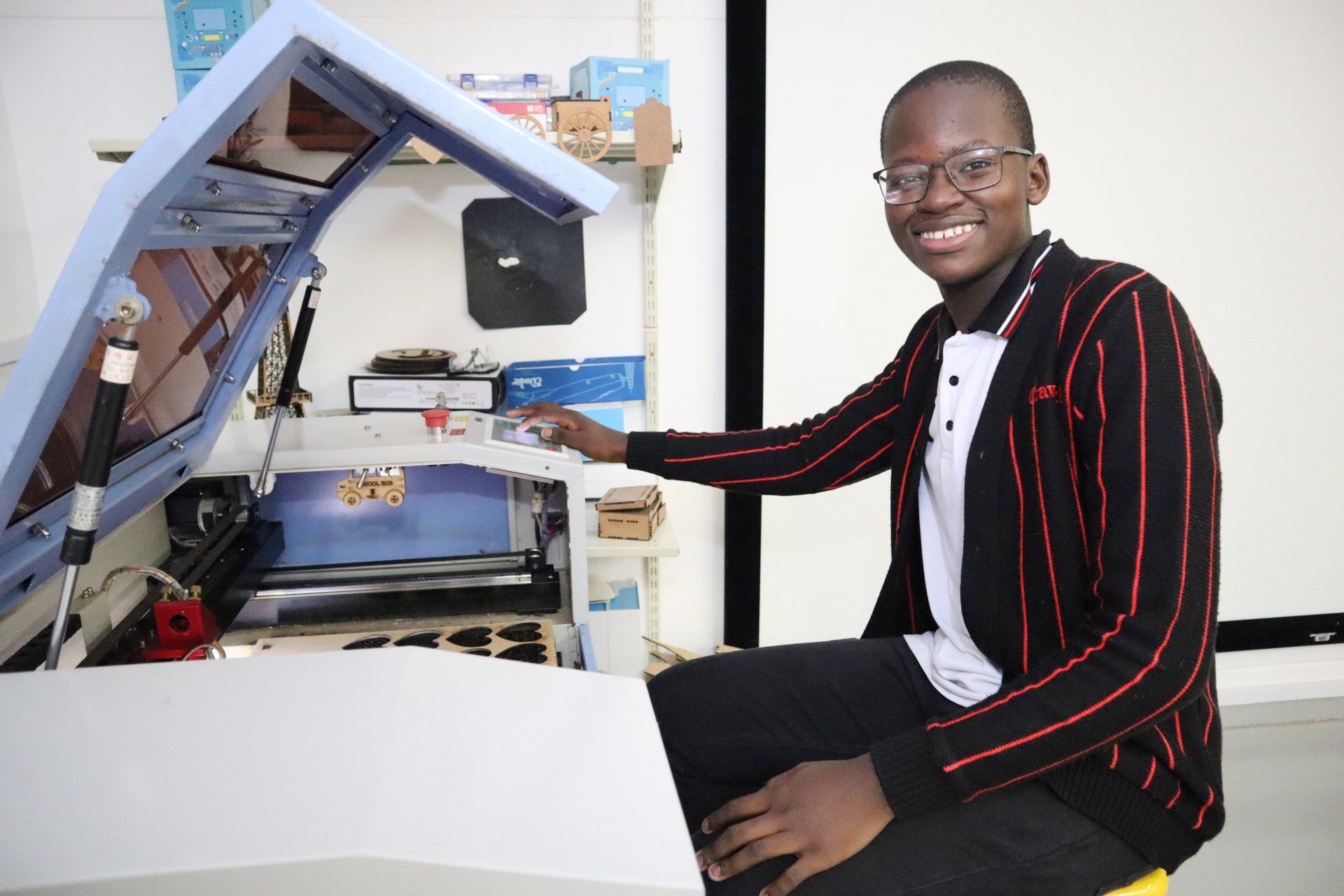a boy in a striped jacket is sitting in front of a laser cutter