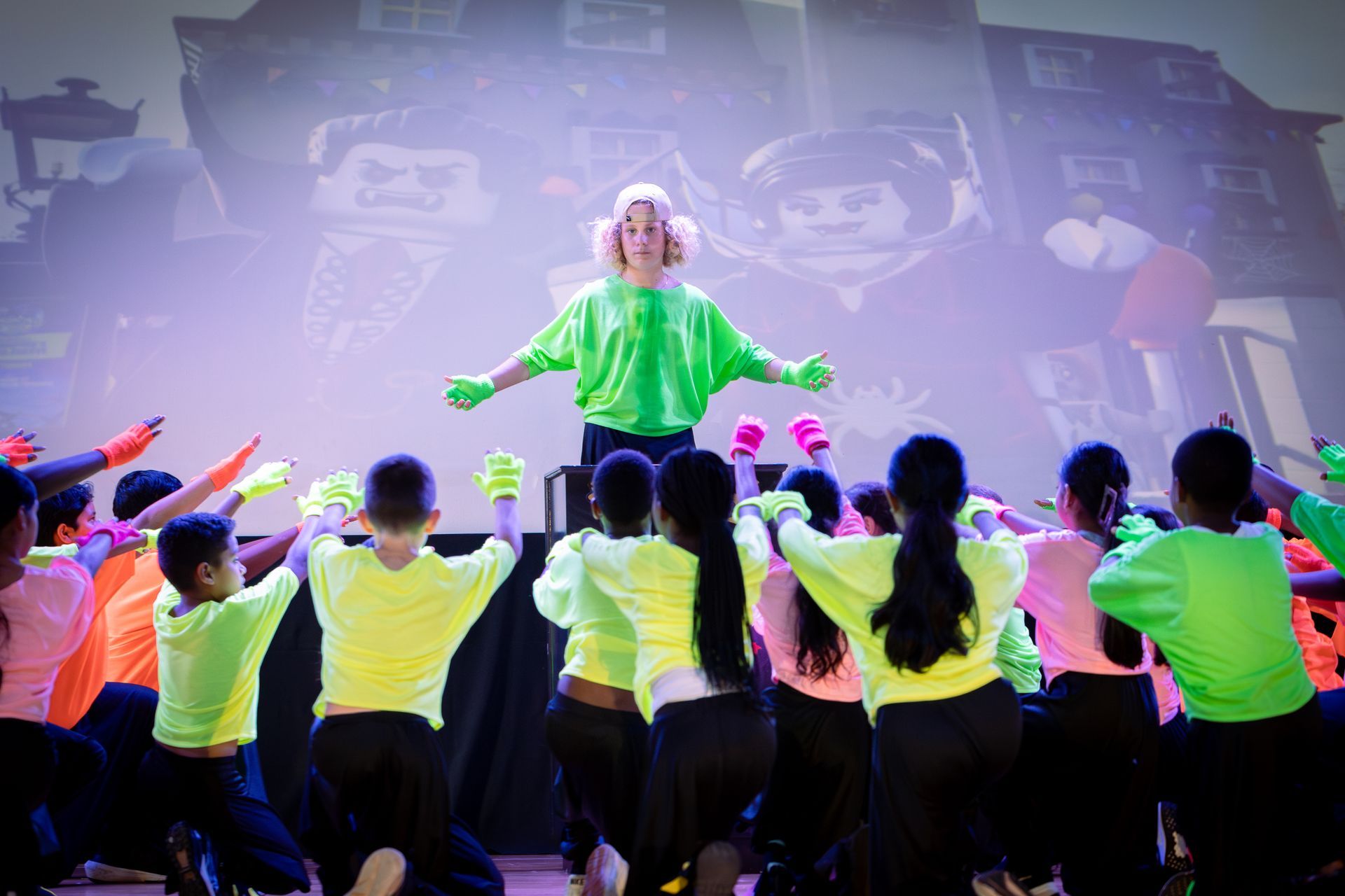A woman in a green shirt is standing in front of a group of children in neon clothes.
