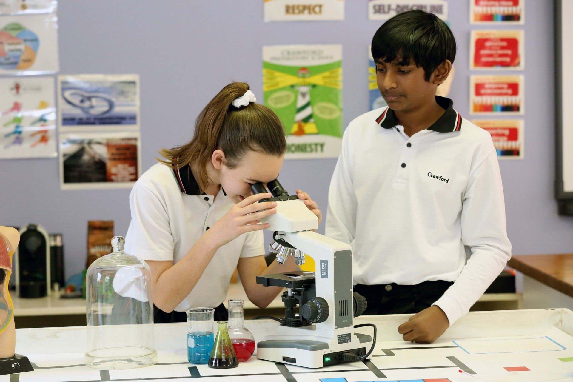 a boy and a girl are looking through a microscope in a classroom .