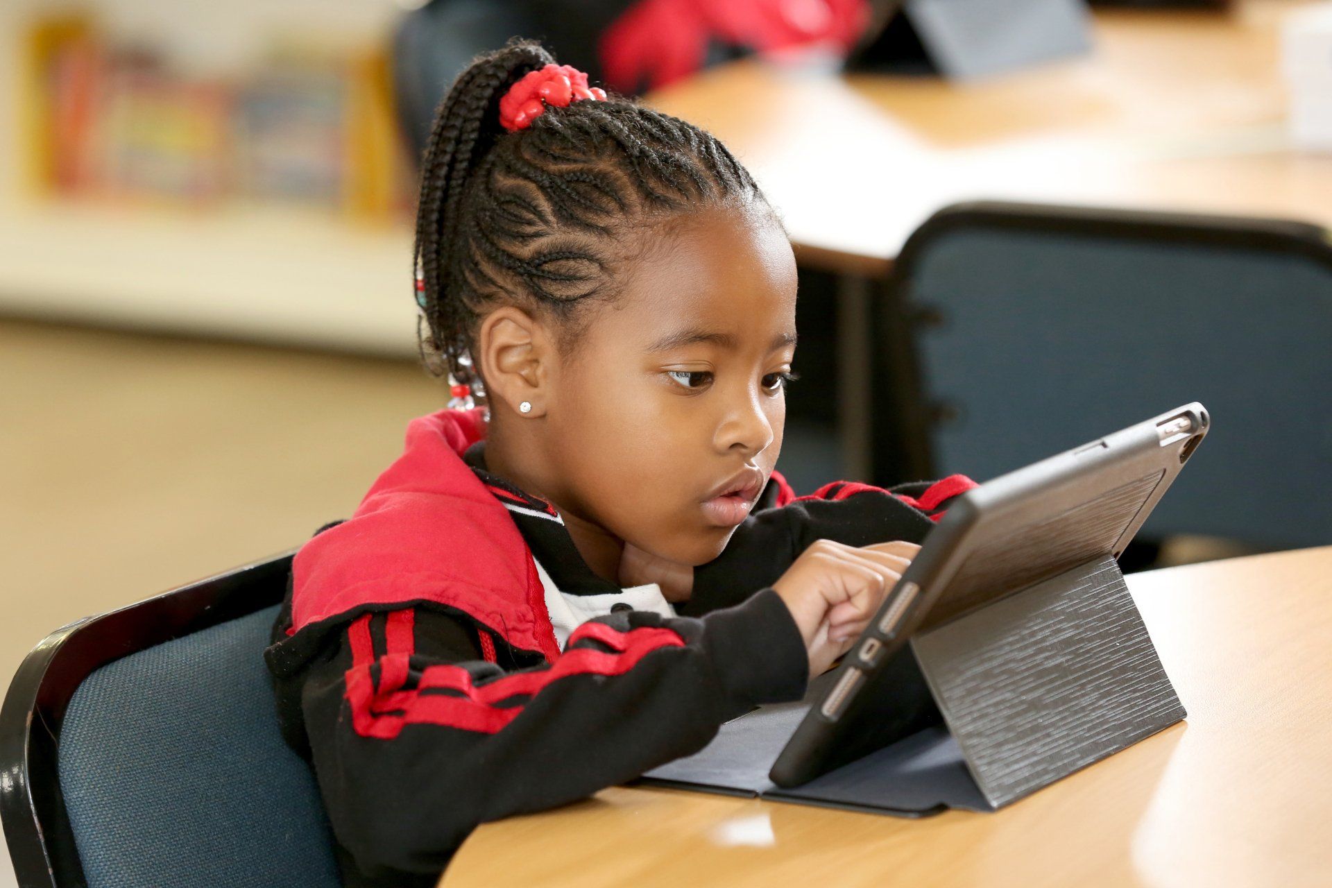 a young girl is sitting at a table using a tablet computer .