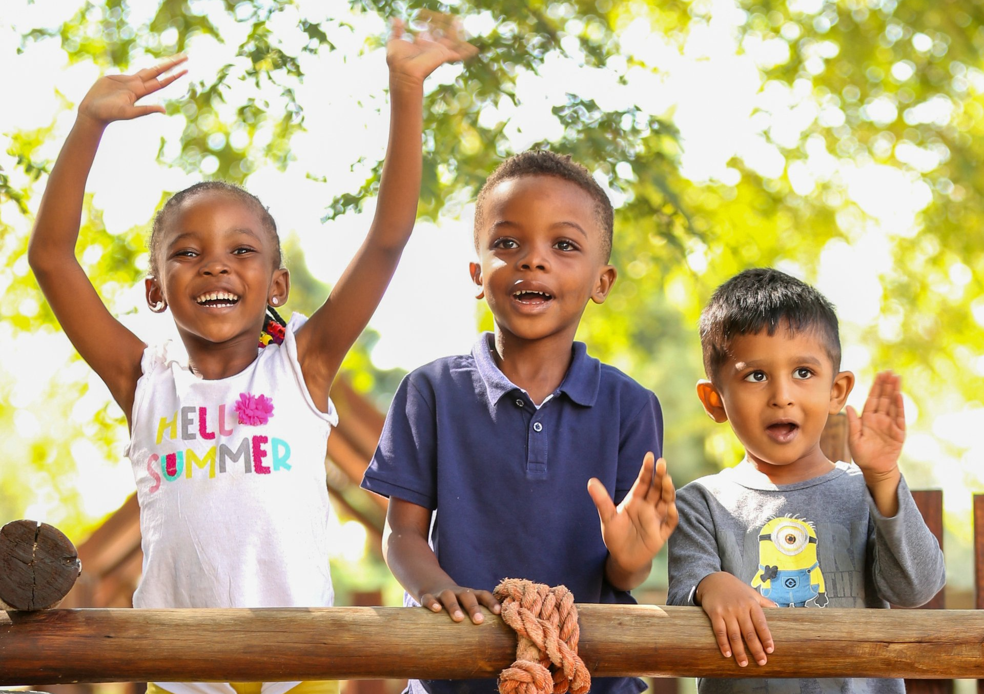 three children are standing next to each other on a wooden fence .