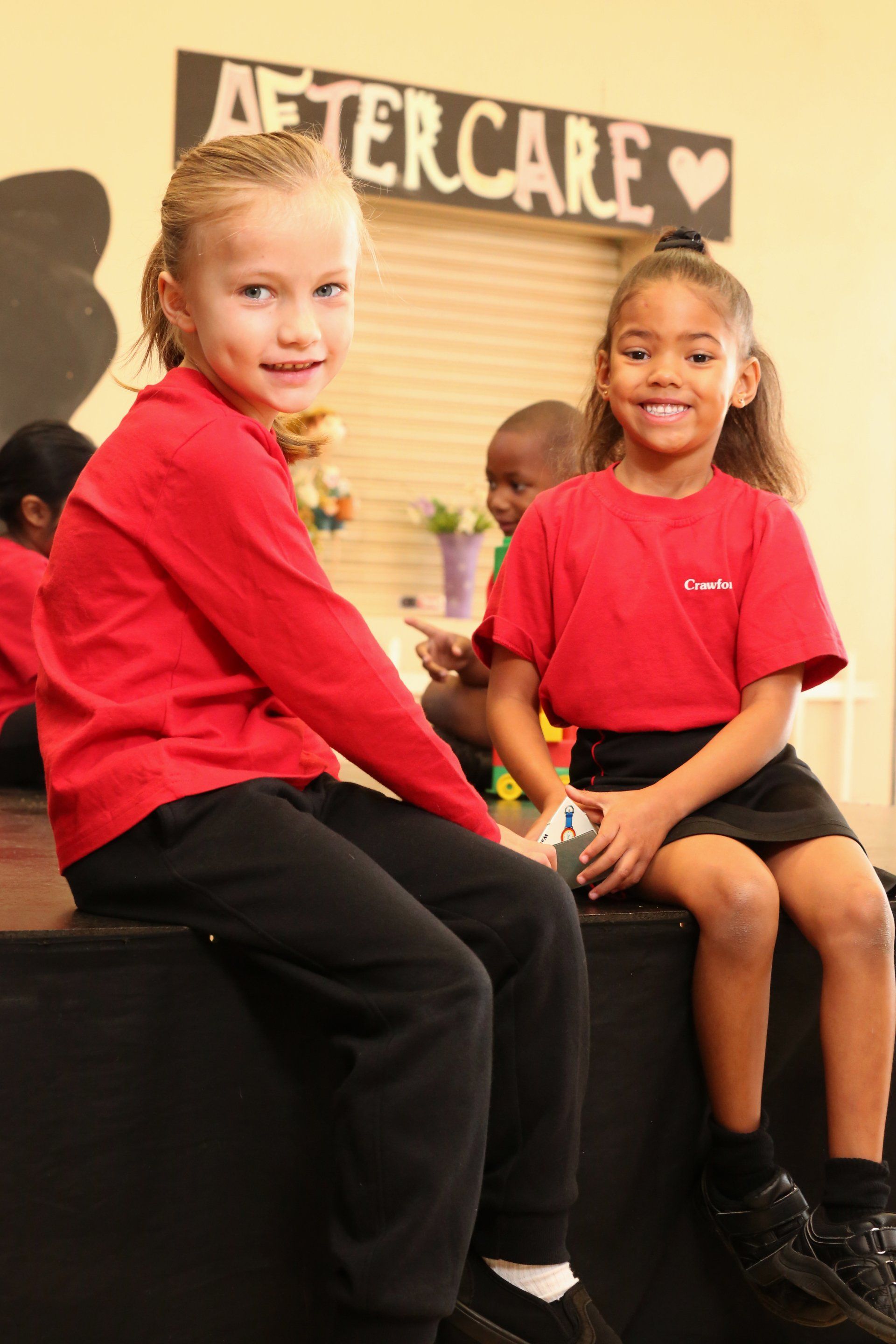 two young girls are sitting on a bench in front of a sign that says aftercare .