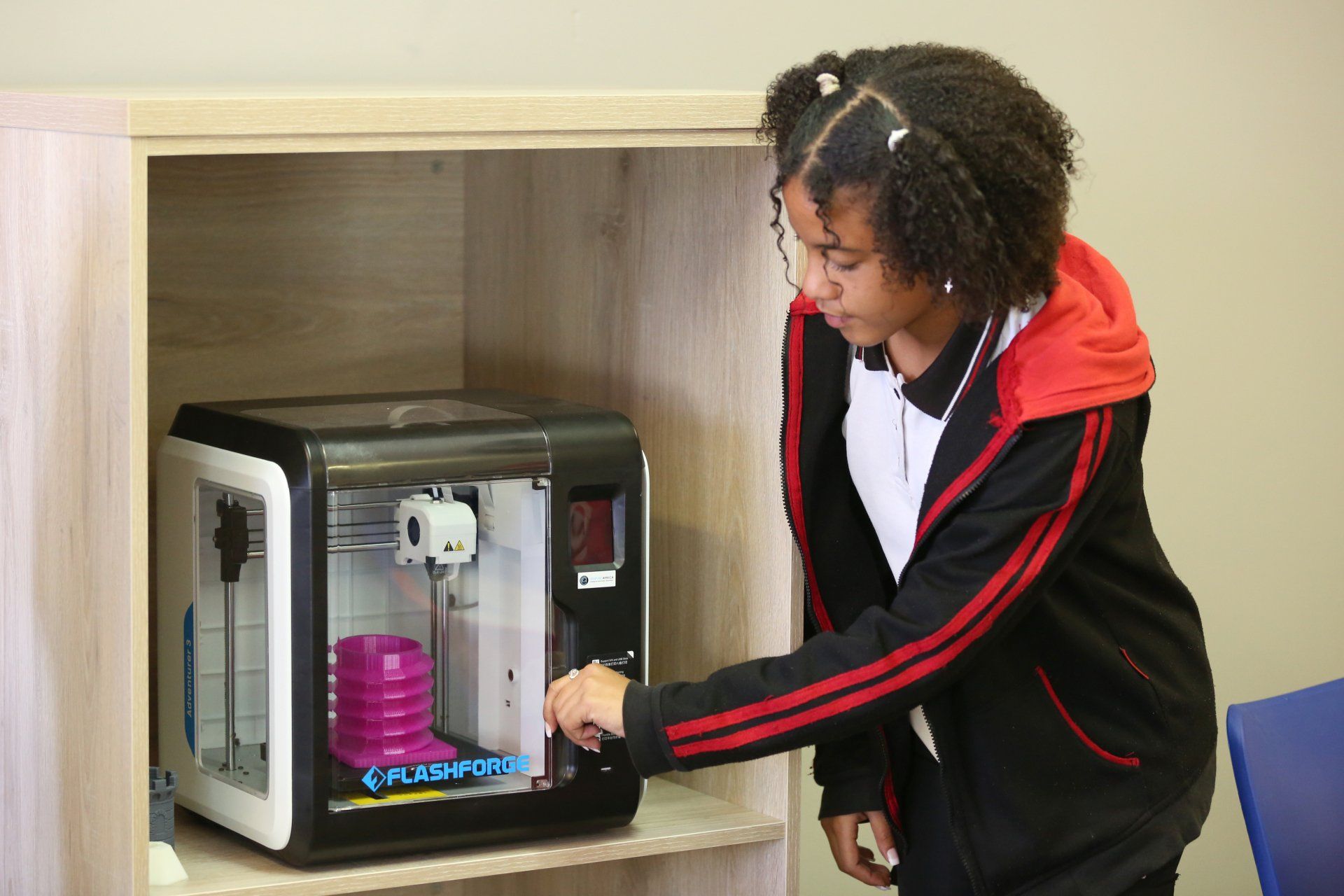 A young woman is using a 3d printer on a shelf.