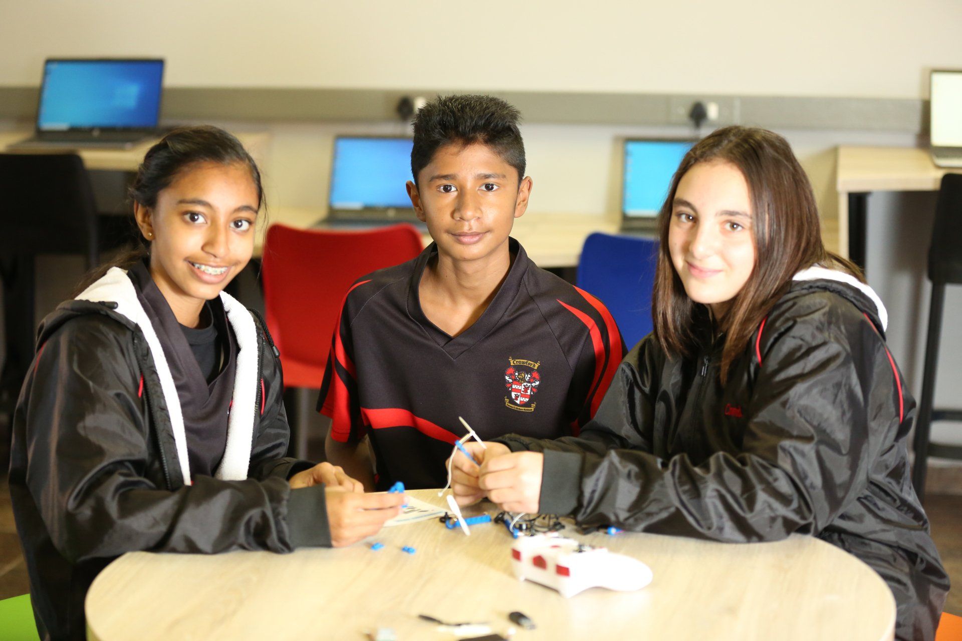 a boy and two girls are sitting at a table in a classroom .