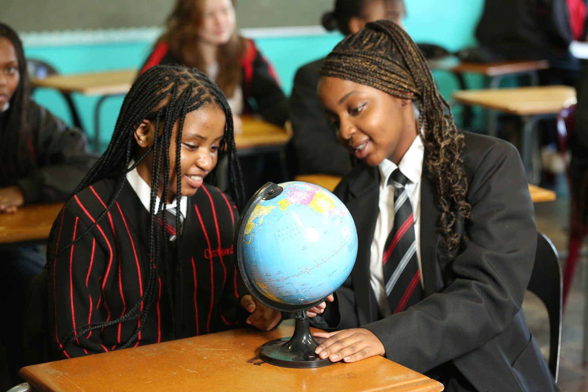 Two students in school uniforms examine a globe at a desk.
