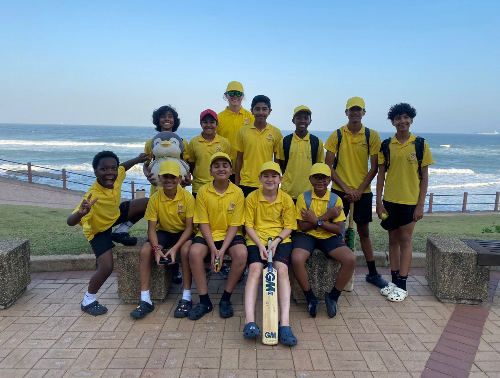 A group of young boys in yellow shirts are posing for a picture in front of the ocean.