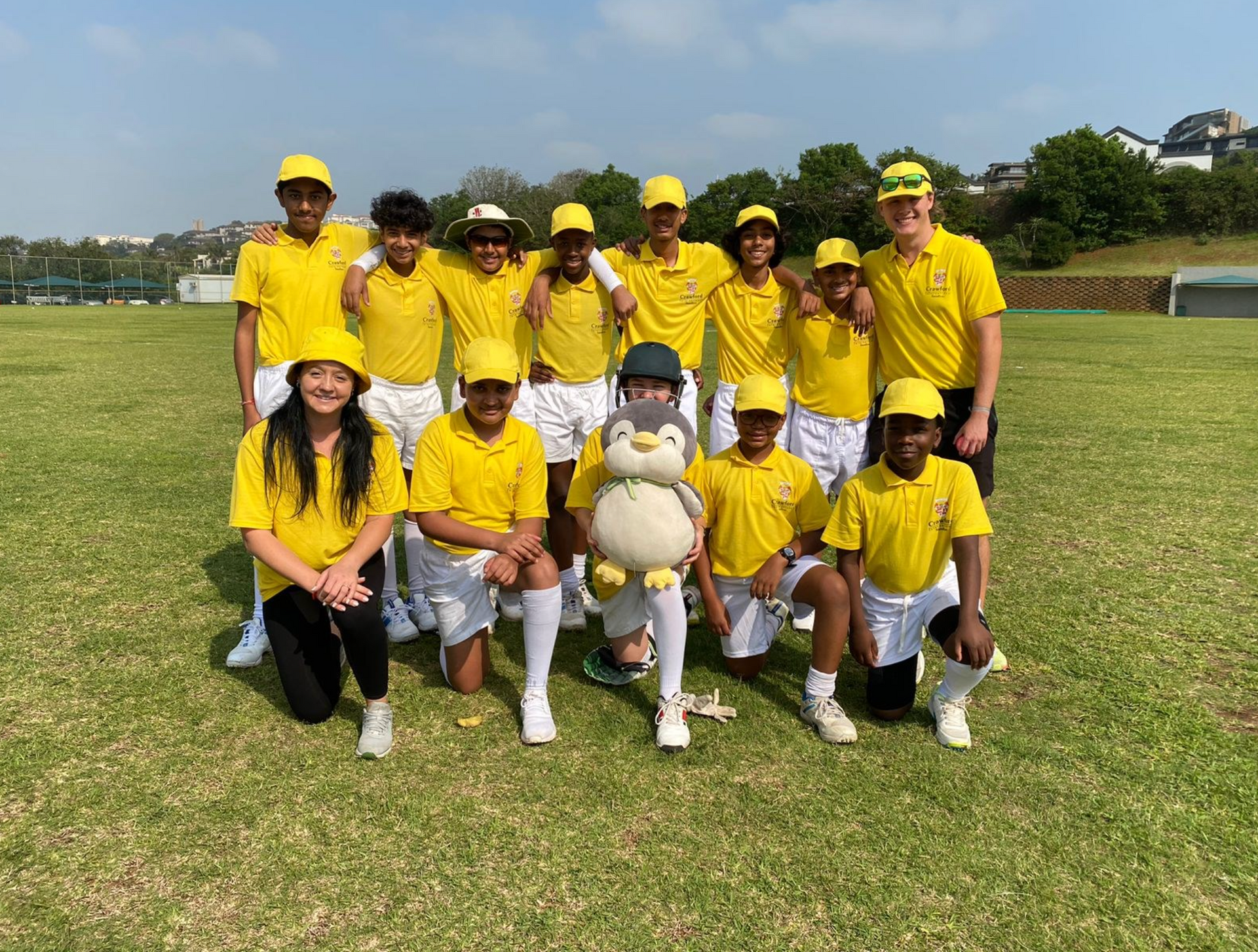 A group of people in yellow shirts are posing for a picture with a stuffed penguin.