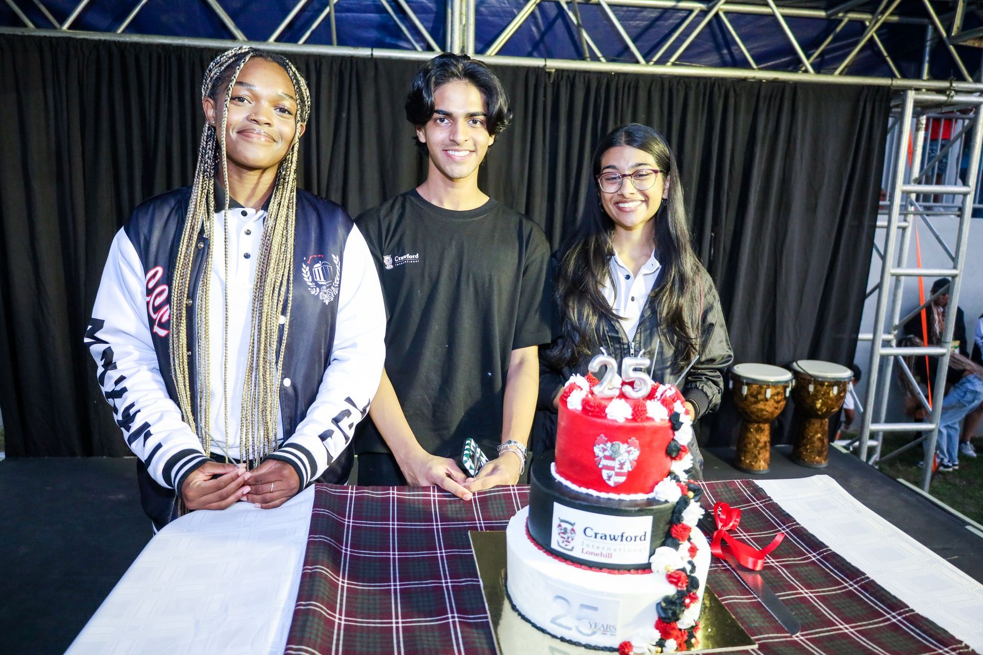 Three people are standing next to a cake on a table.