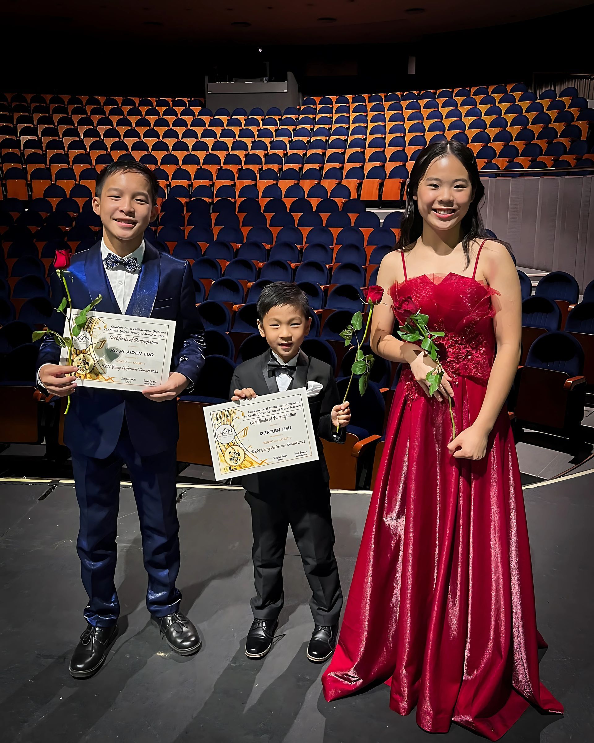 A boy in a suit and a girl in a red dress are standing next to each other on a stage.
