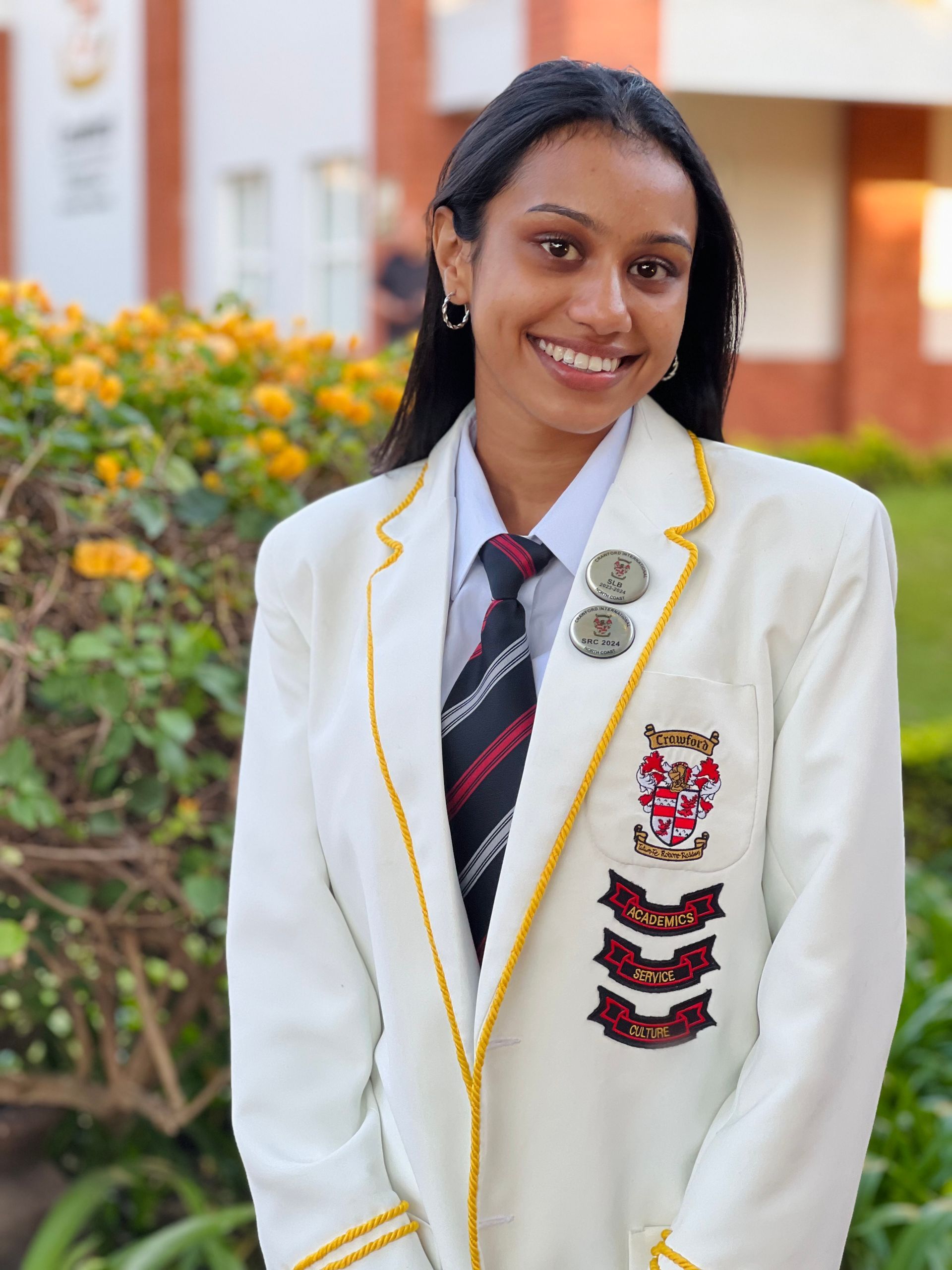 A young woman wearing a white jacket and tie is smiling.