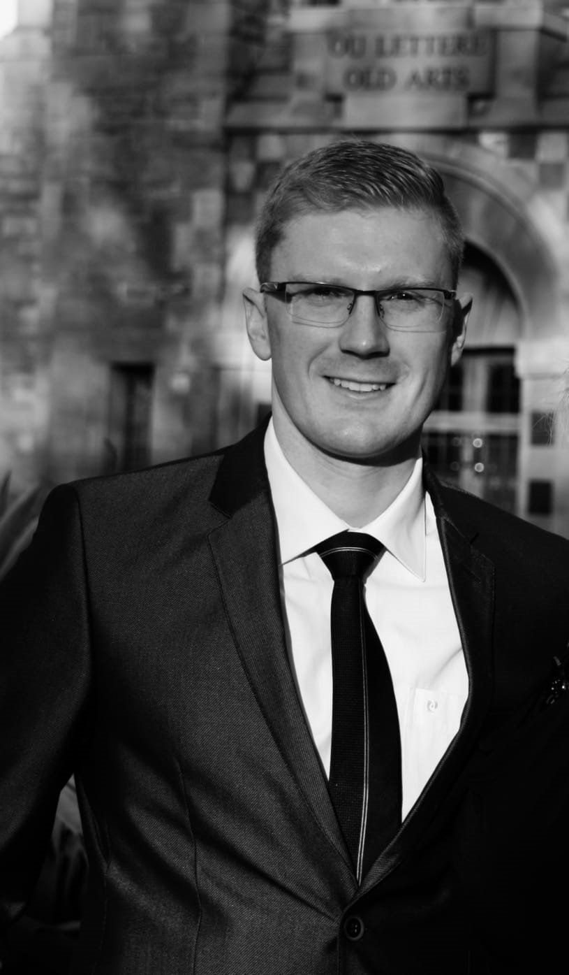 A man in a suit and tie is smiling in a black and white photo.