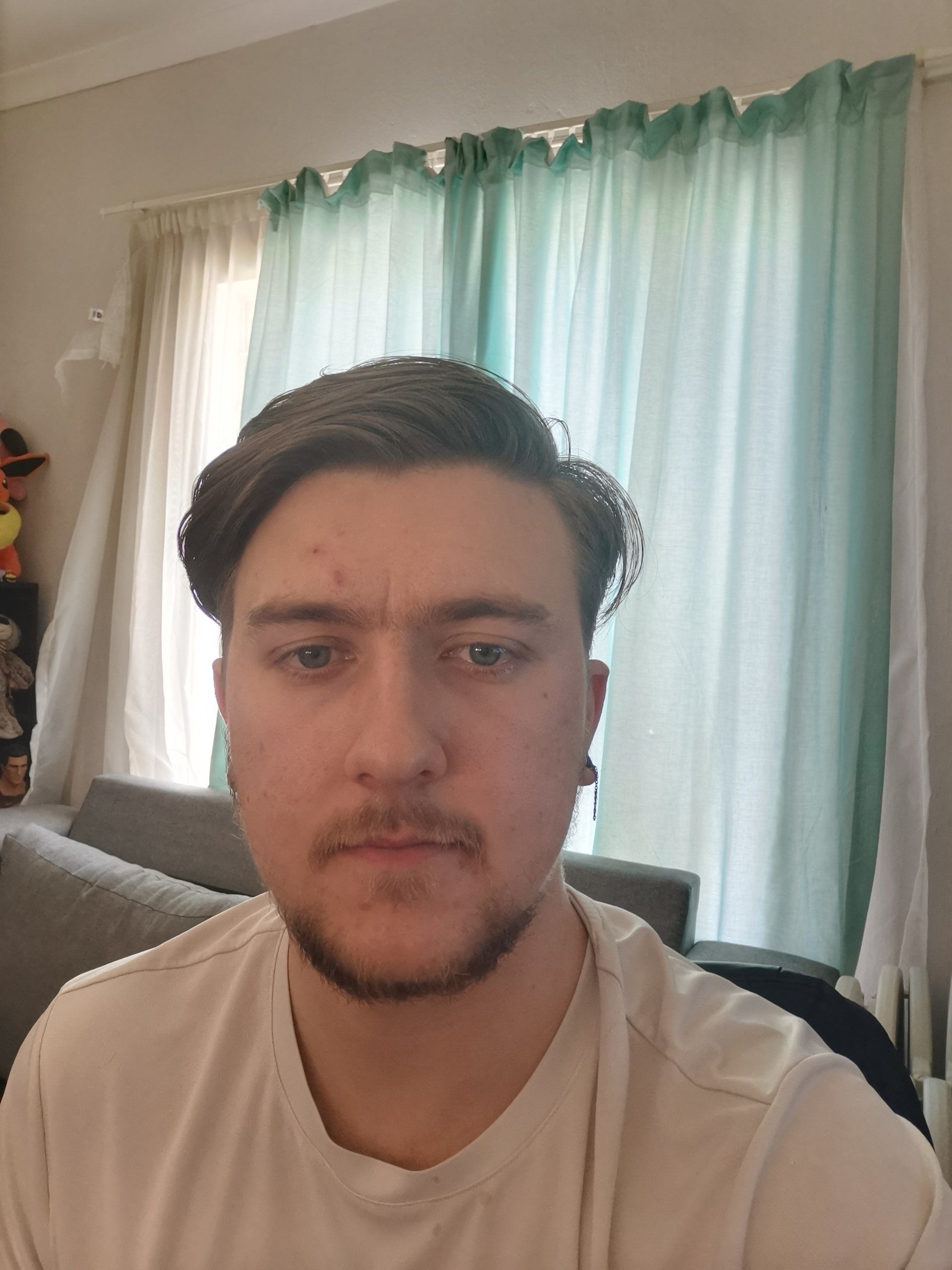 A man with a beard is taking a selfie in a living room.