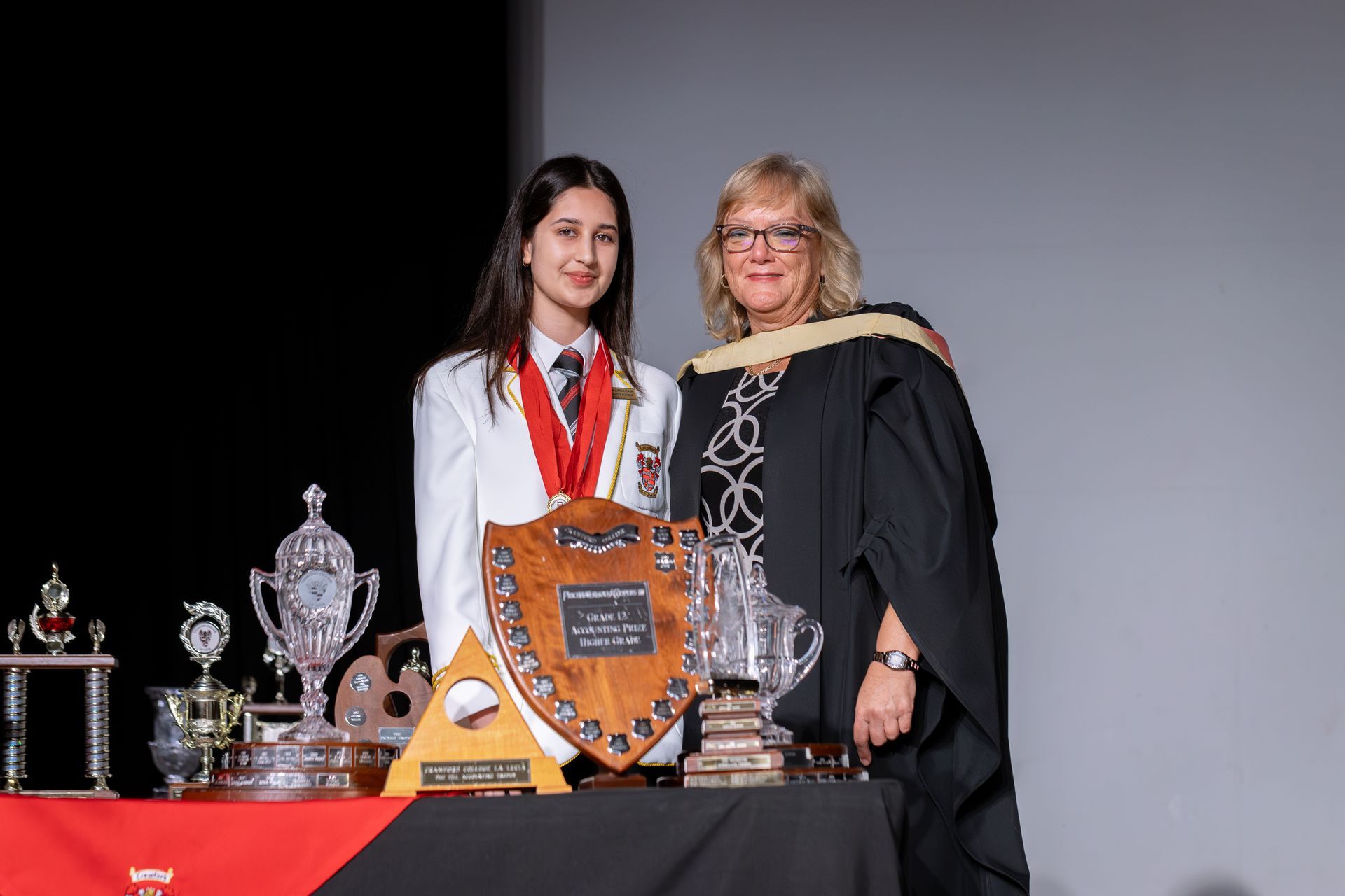Two women are standing next to each other on a stage holding trophies.