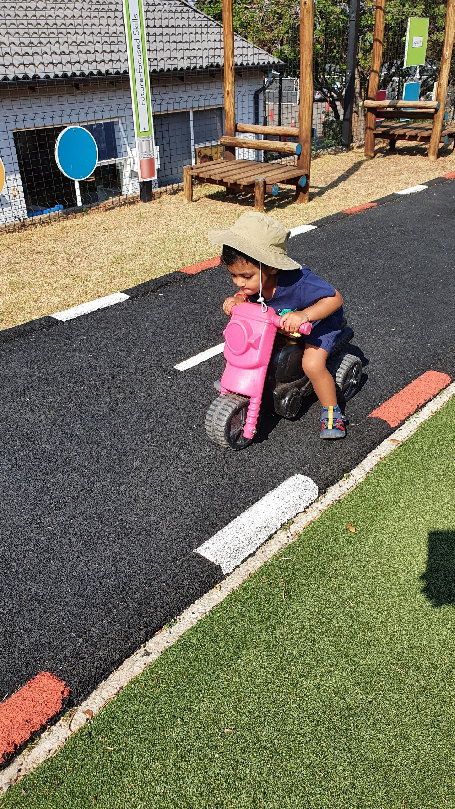 A little boy is riding a pink tricycle on a road.