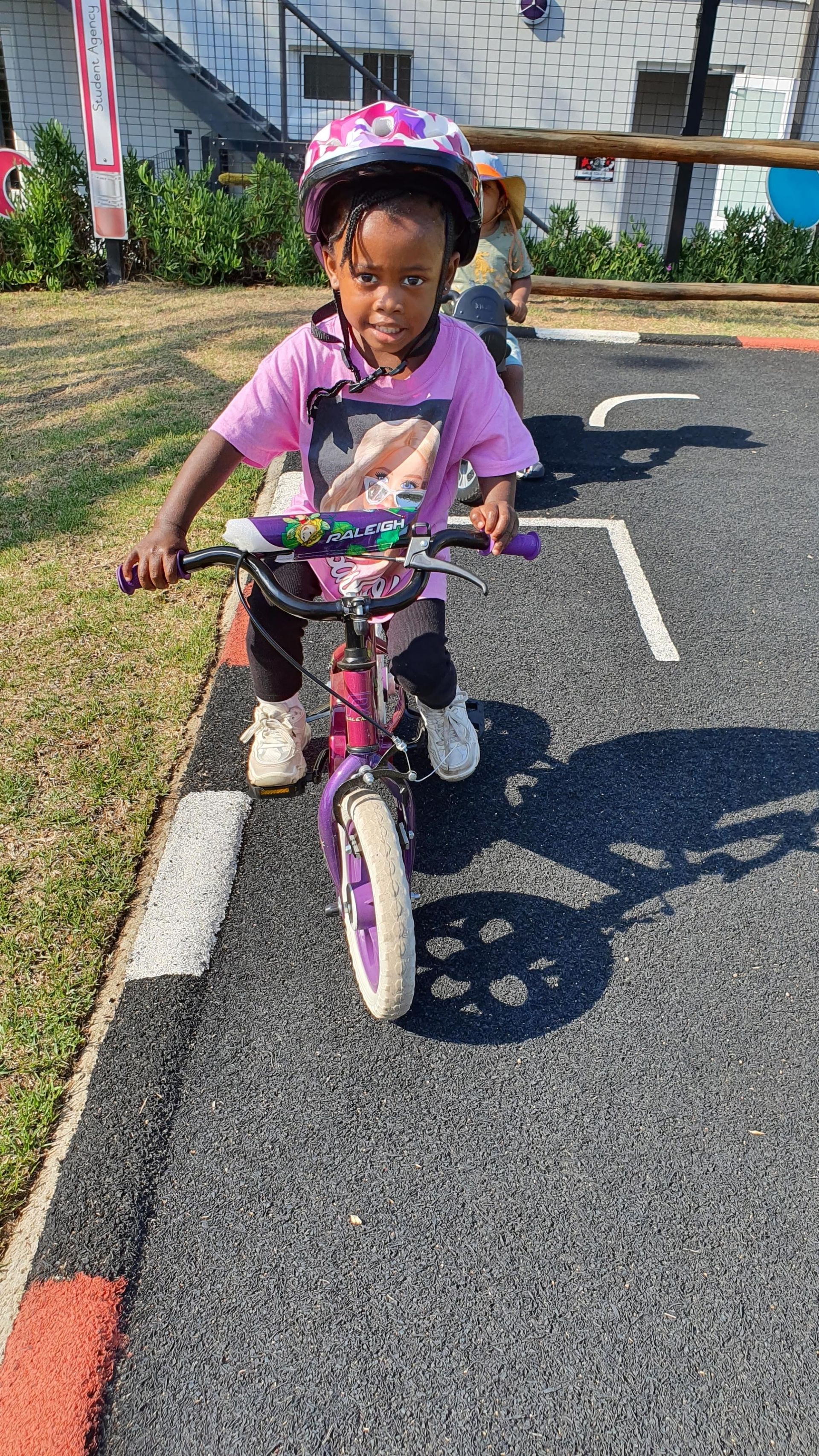 A little girl is riding a purple bike on a road.