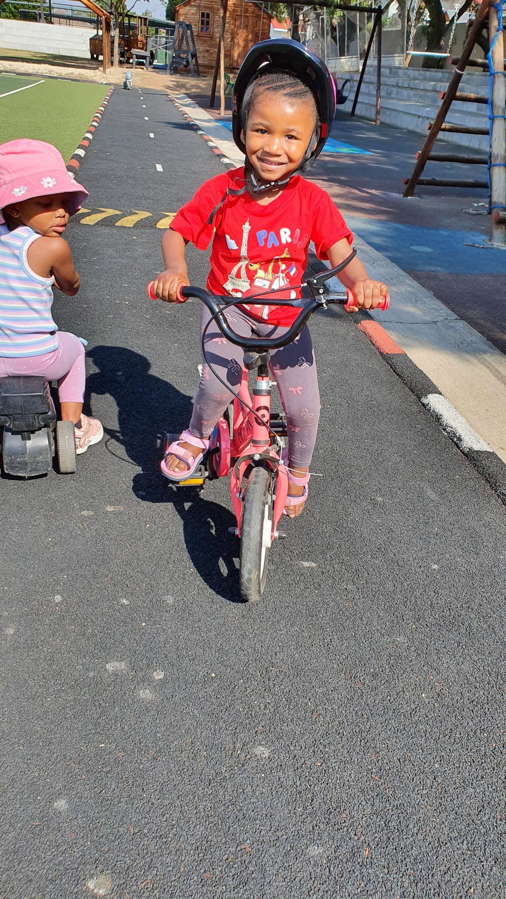A little boy is riding a bike next to a little girl on a tricycle.