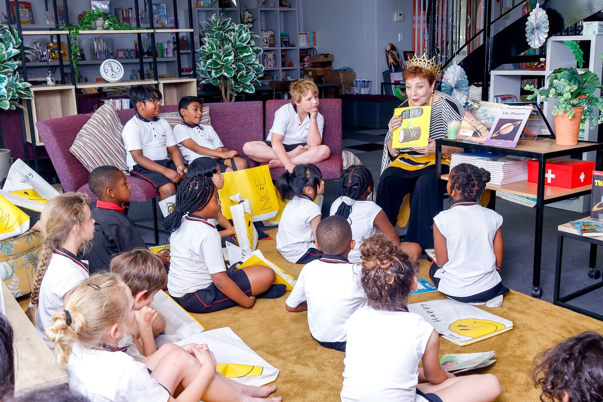 a group of children are sitting on the floor listening to a teacher read a book .