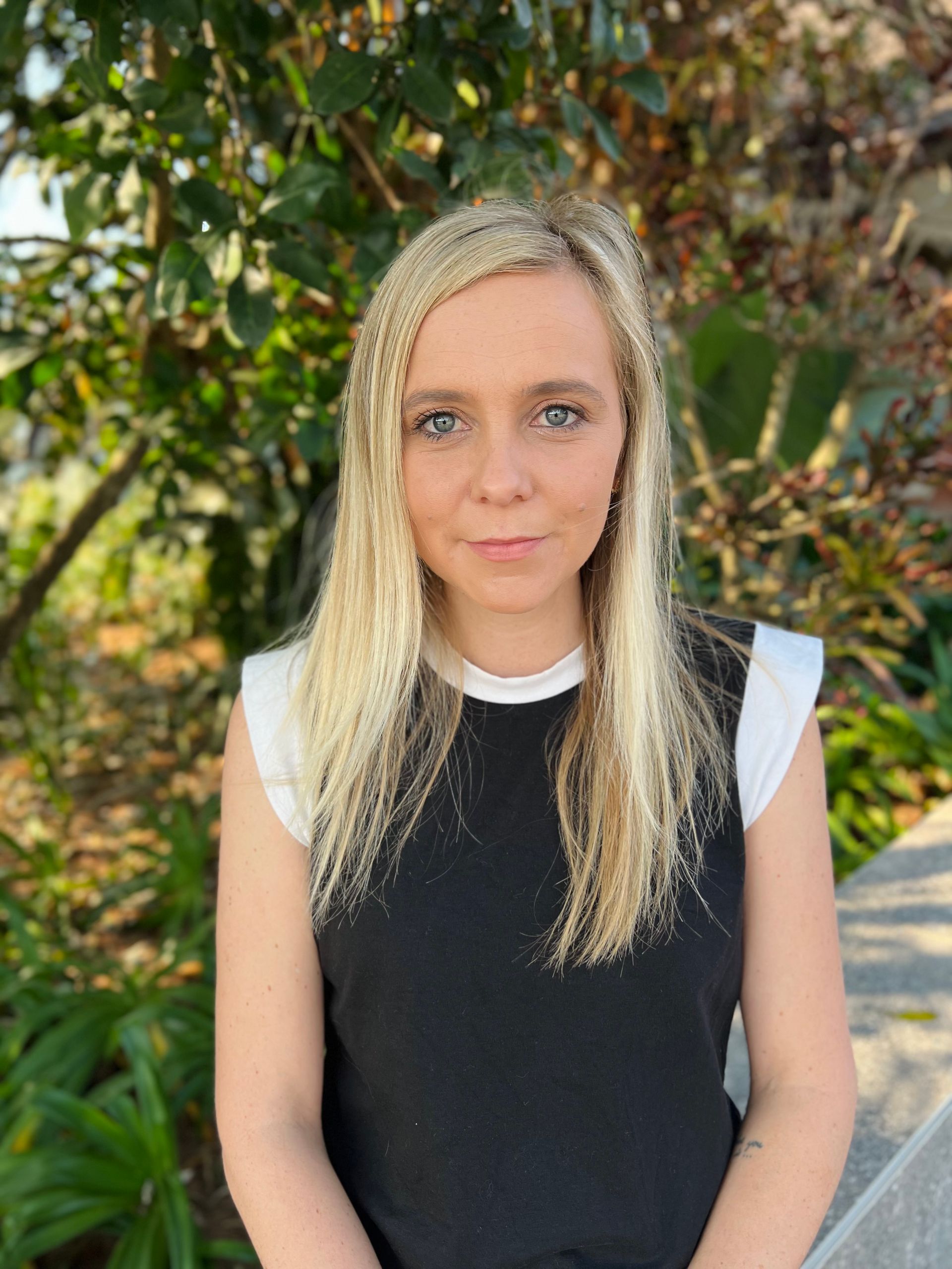 A woman with blonde hair is wearing a black vest and a white shirt.
