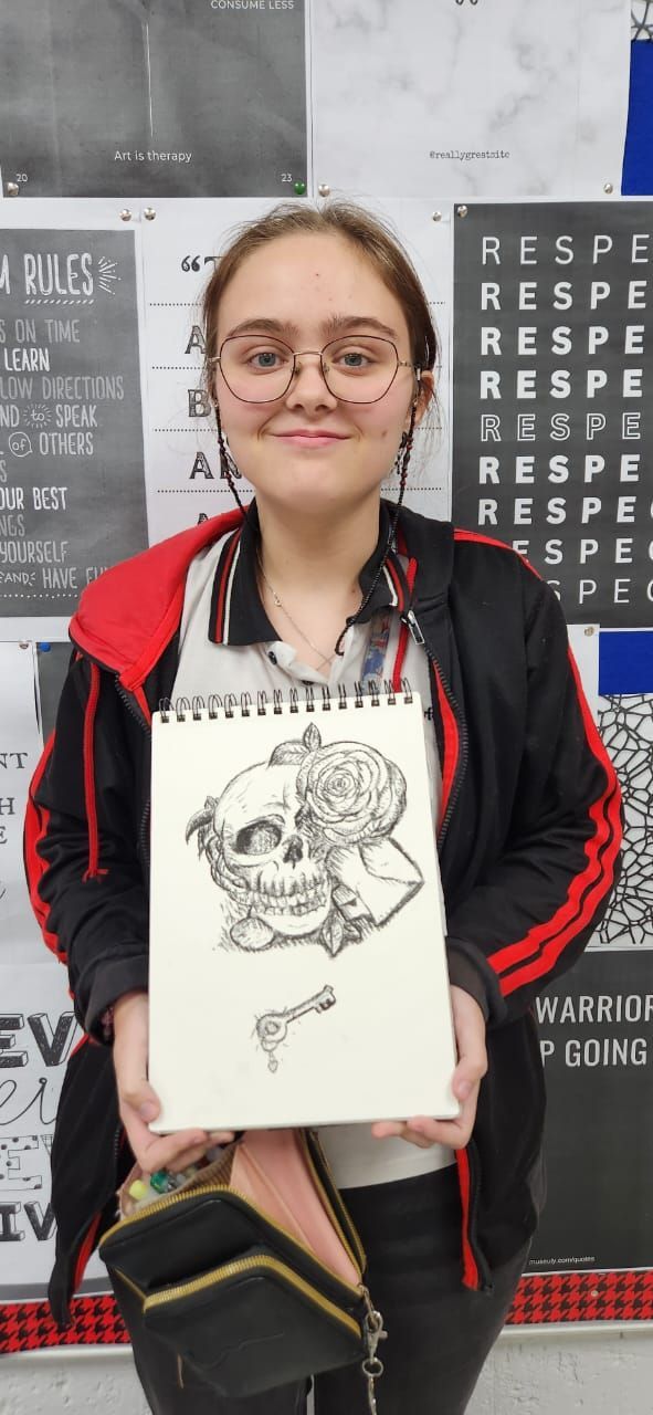 A girl is holding a drawing of a skull in a notebook.