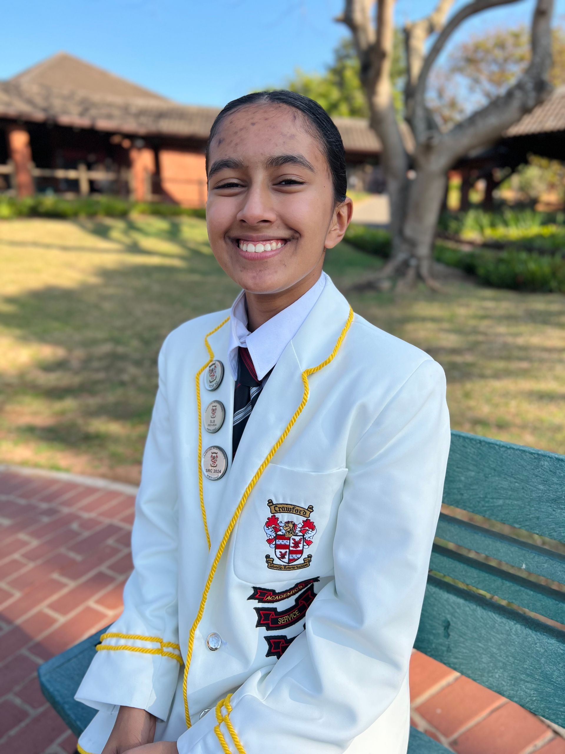 A girl in a white suit is sitting on a bench and smiling.