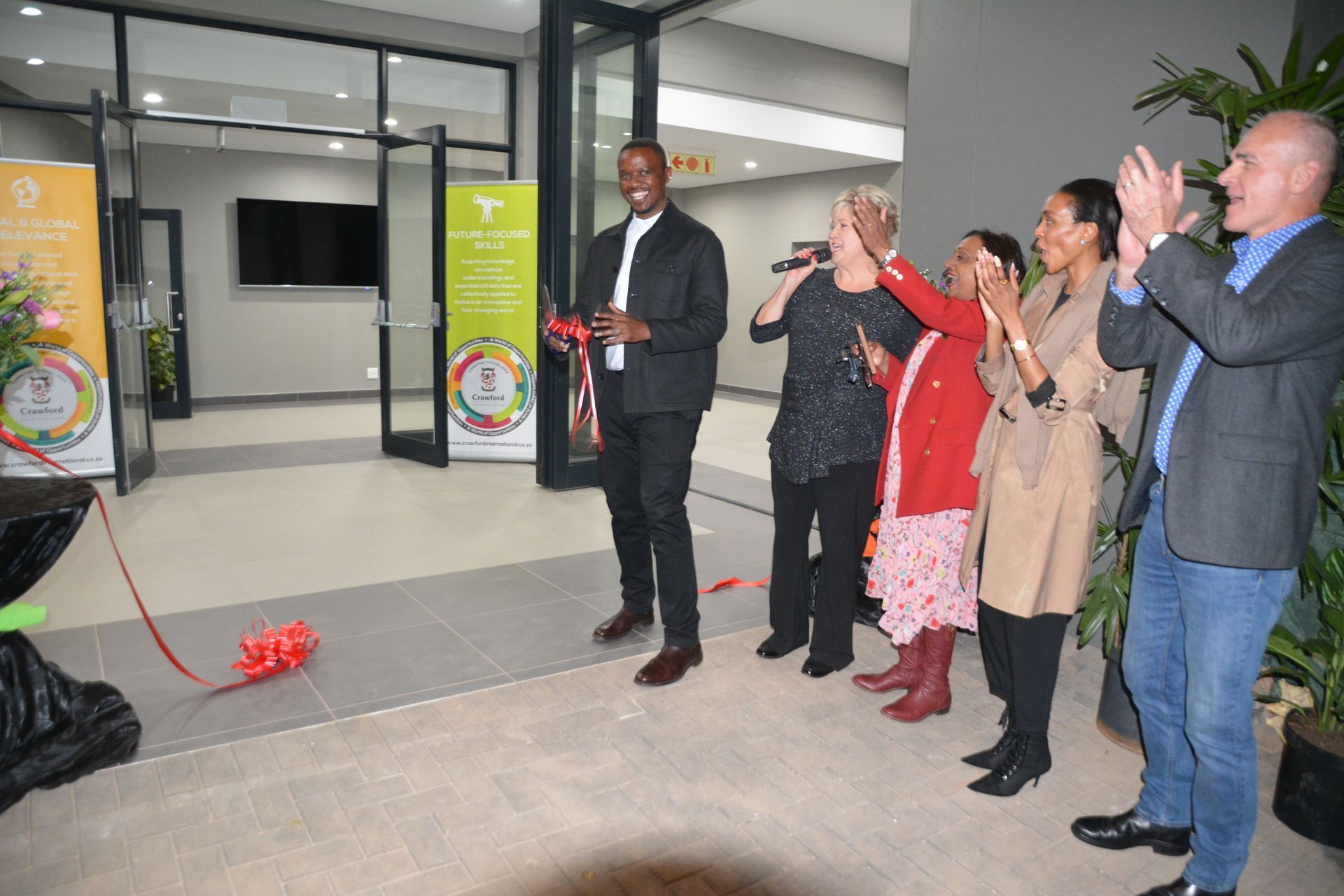 A group of people are standing around a man cutting a red ribbon.