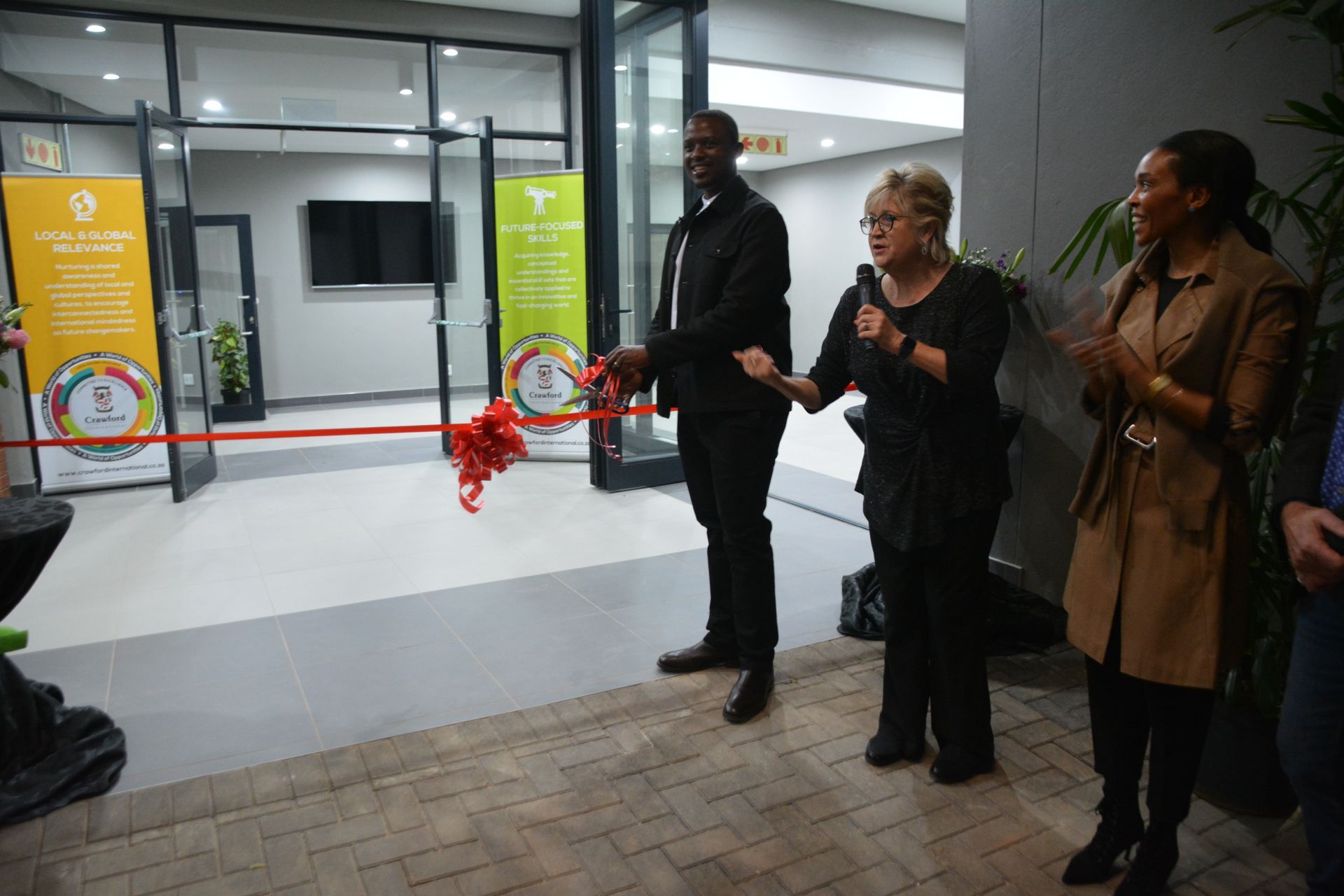 A man and woman are cutting a red ribbon in front of a building.