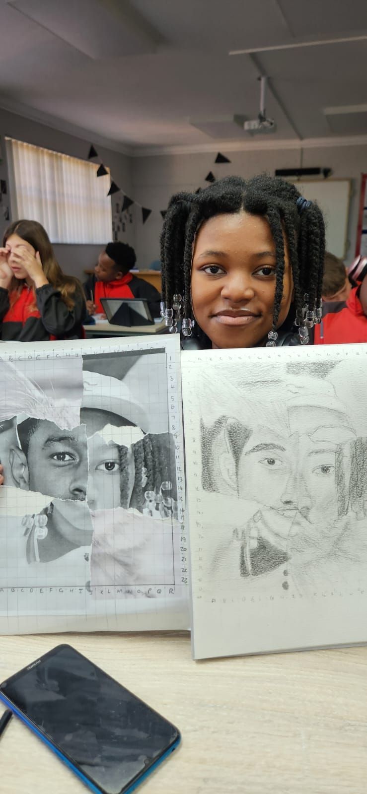 A woman is sitting at a table with two drawings on it.