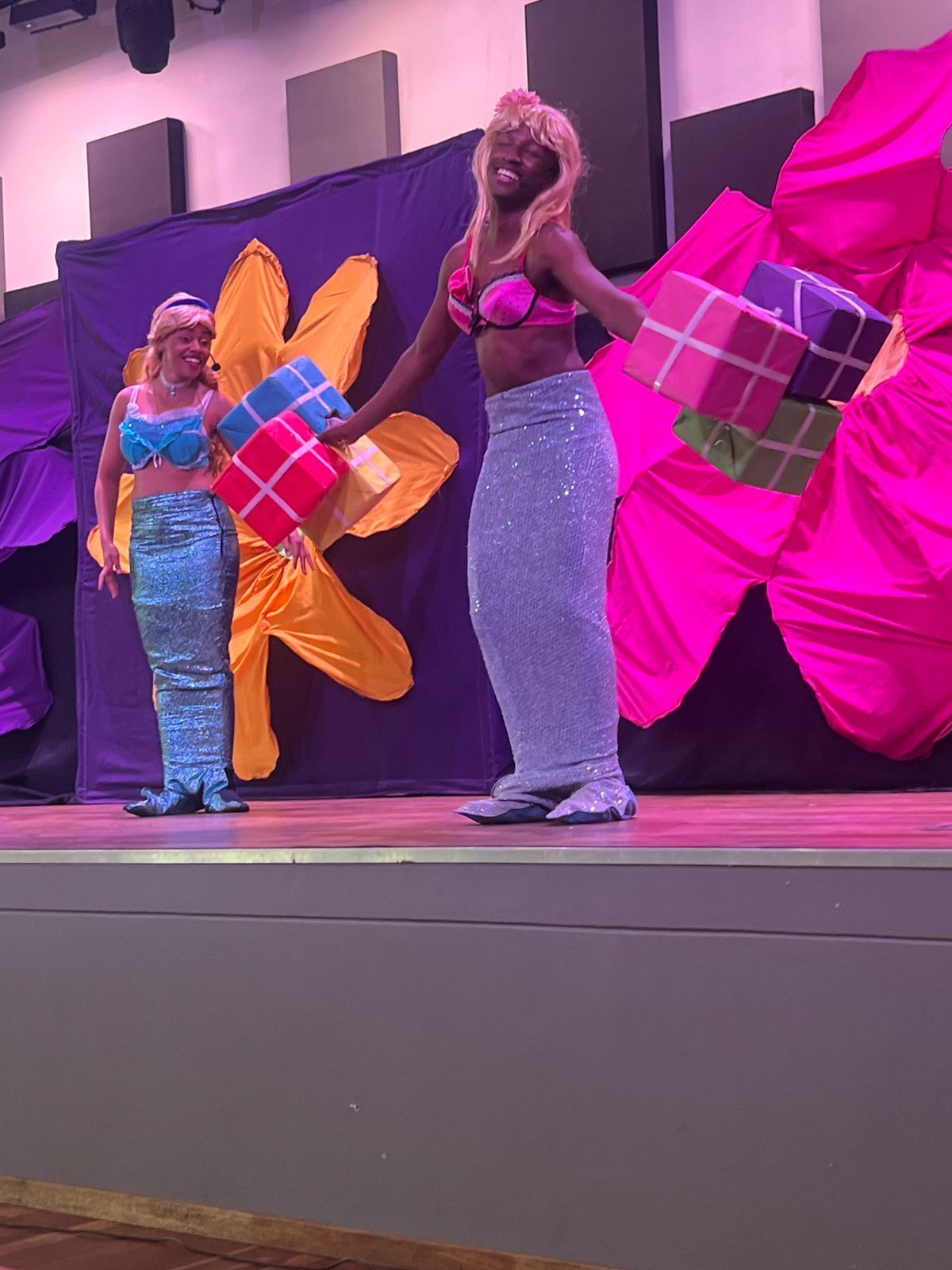 Two women dressed as mermaids holding presents on a stage